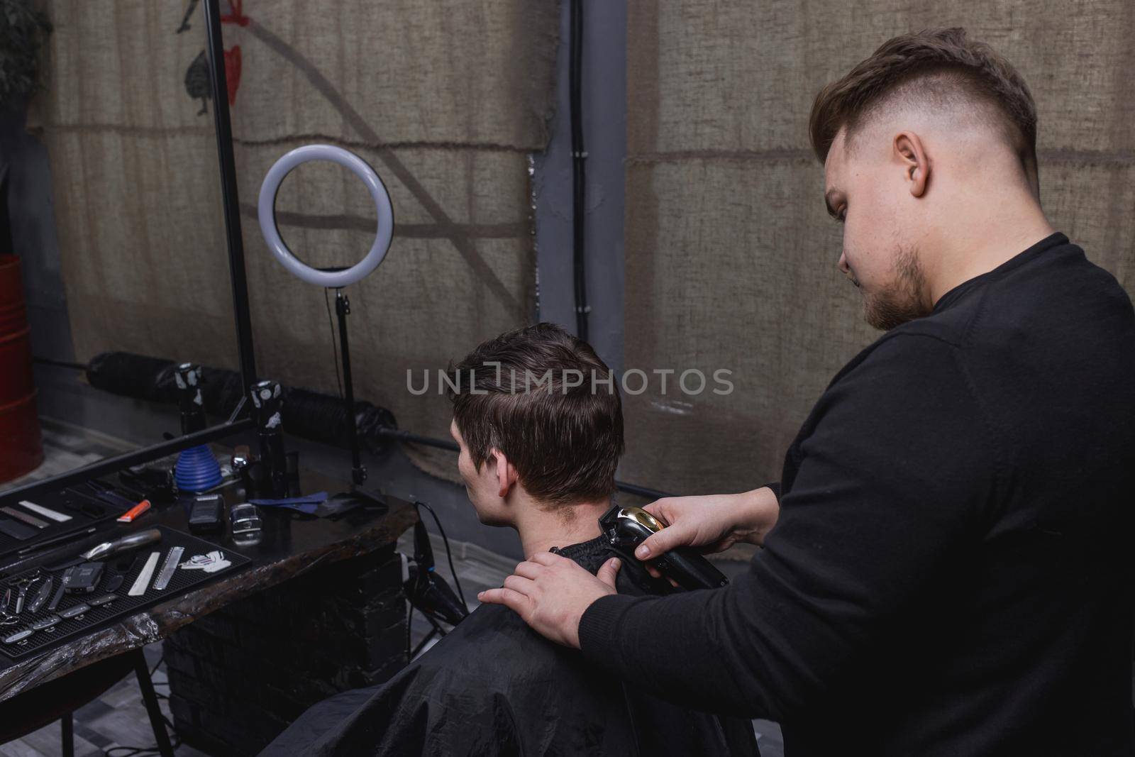 Barber or hairdresser cuts the back of the head of a guy with dark hair with a machine. Hairdressing by AYDO8