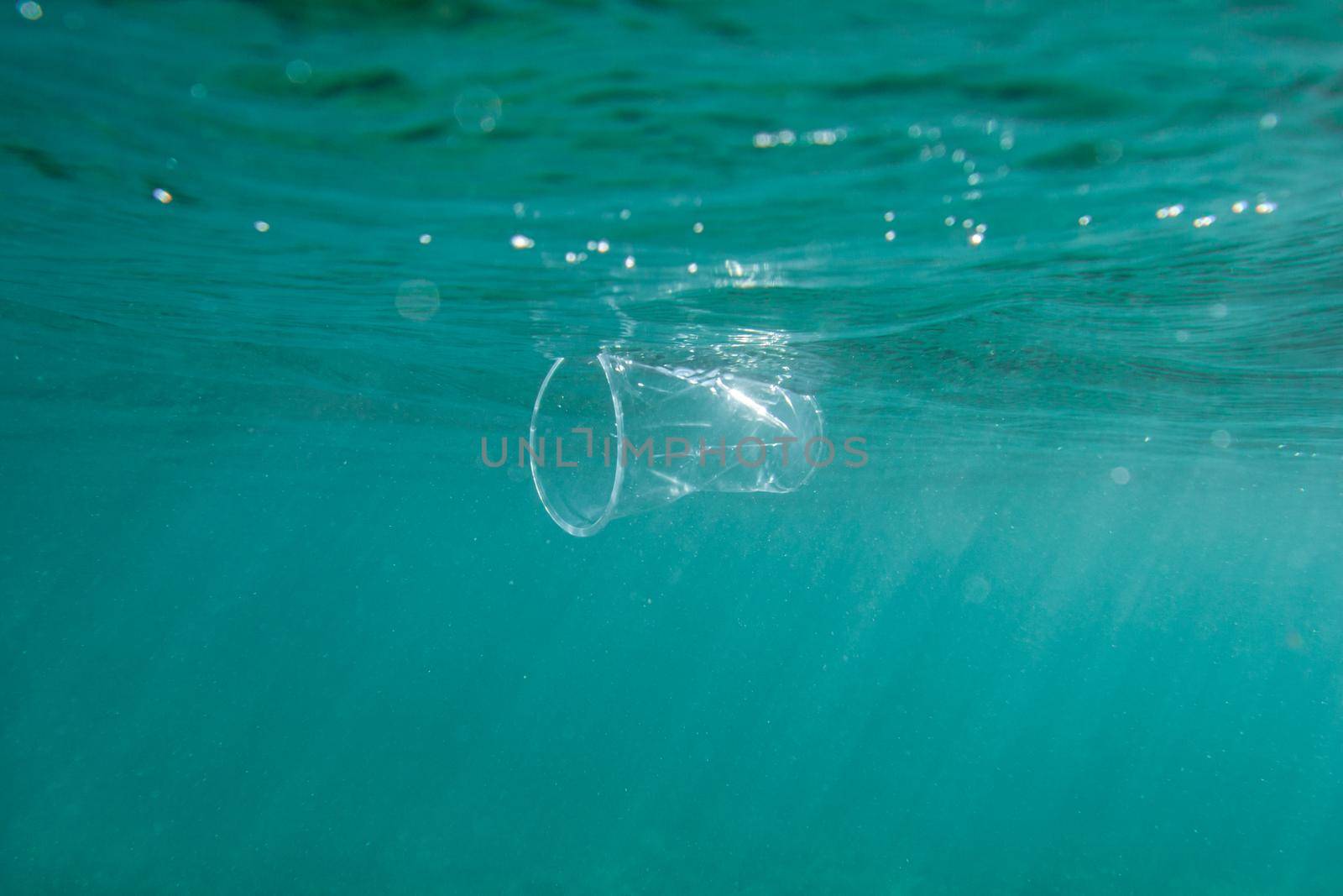 Plastic cup floats underwater in the open ocean. Environmental pollution concept.
