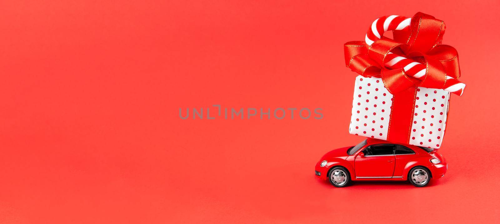 Moscow, Russia, January 14, 2021. Banner minimal design for celebrating christmas or new year greeting card. Gift delivery concept. Little red toy car with gift and candy on a red background. by chelmicky
