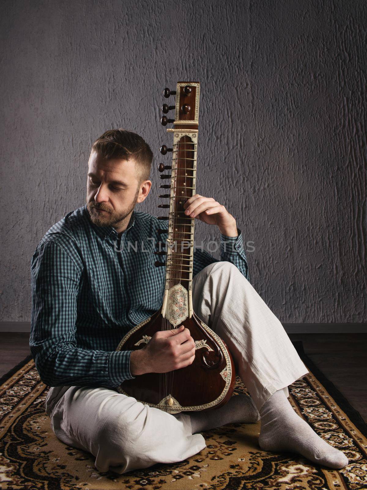 Portrait of a European man playing the sitar sitting on the carpet by zartarn