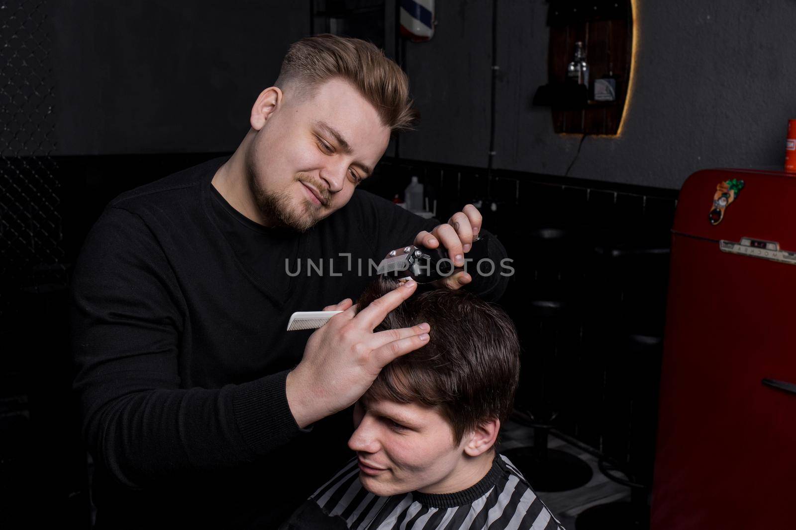 The hands of a barber or hairdresser cut a client with dark hair with an automatic machine and a comb in the barbershop. Hairdressing by AYDO8