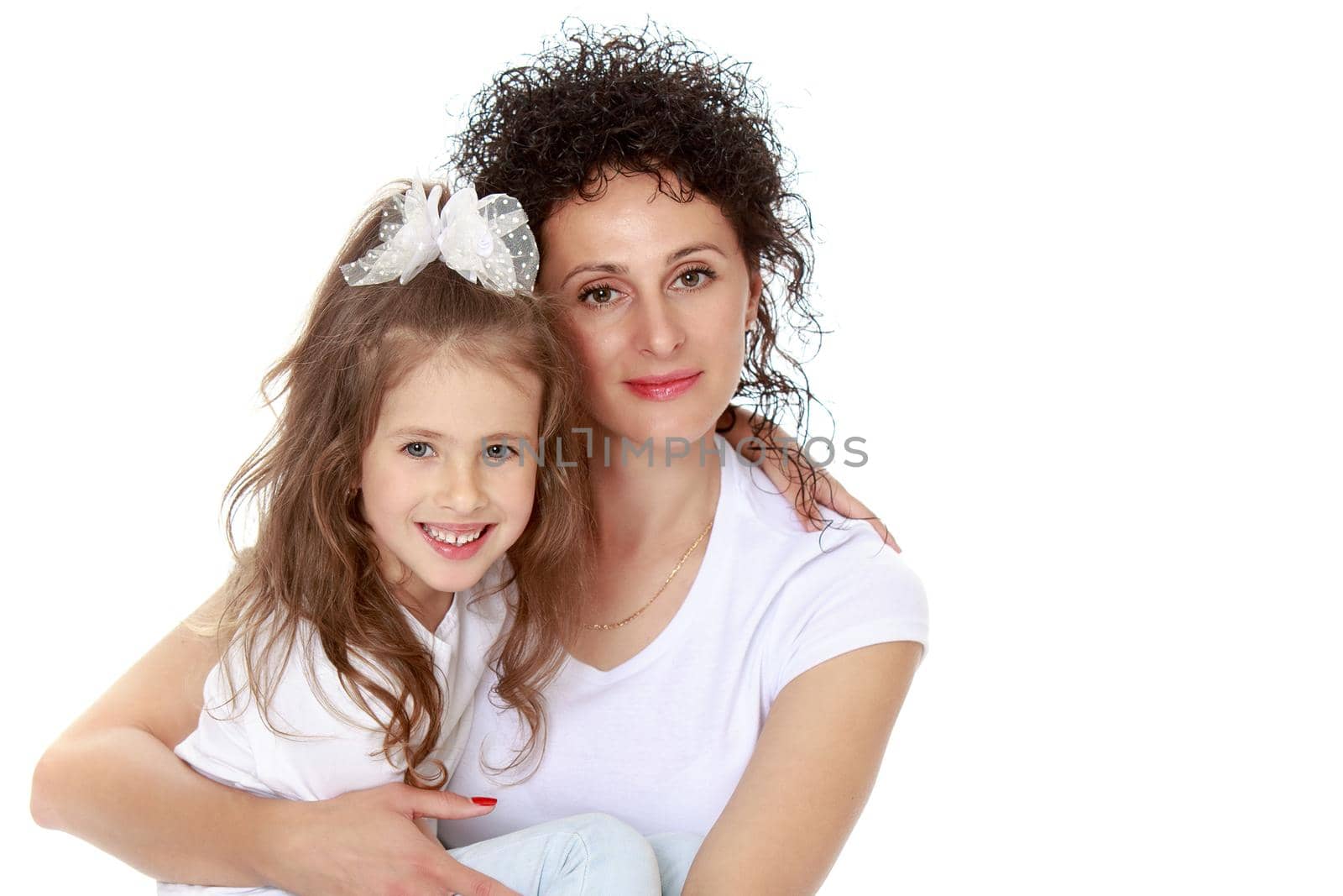 Happy, charming young mother with adorable little daughter. In the same jeans and white t-shirts without a pattern. Mom sits on floor and holds daughter on hands - Isolated on white background