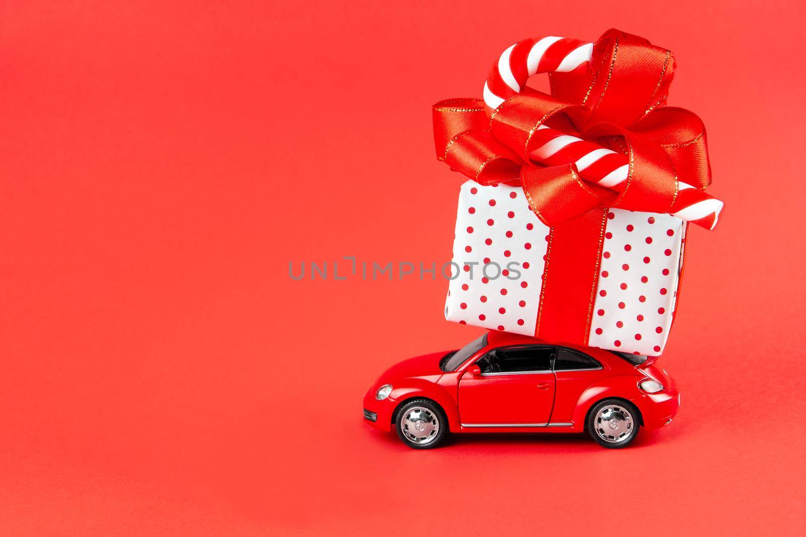 Moscow, Russia, January 14, 2021. Minimal design for celebrating christmas or new year greeting card. Gift delivery concept. Little red toy car with gift and candy on a red background.