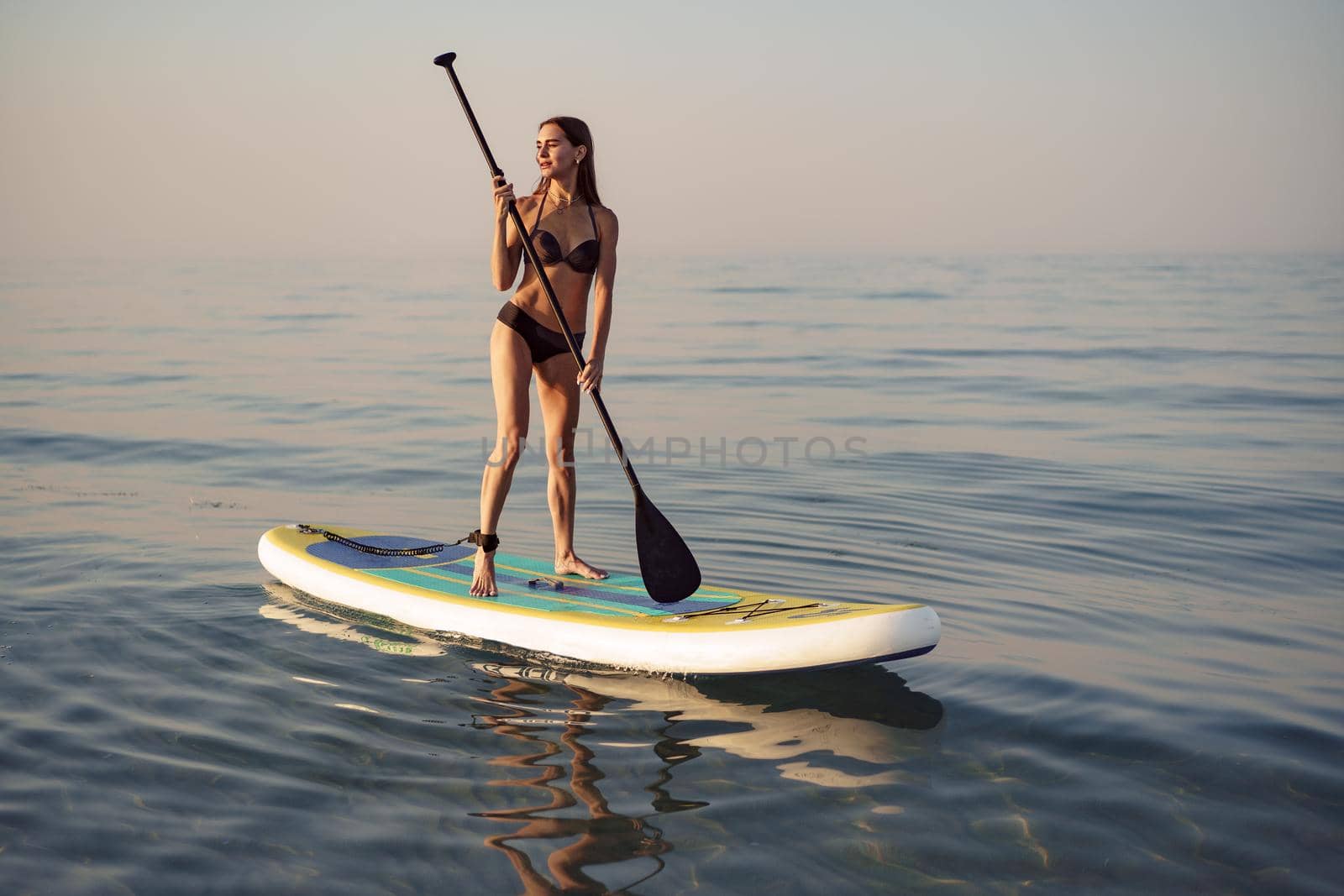 Young attractive woman standing on paddle board at sunrise