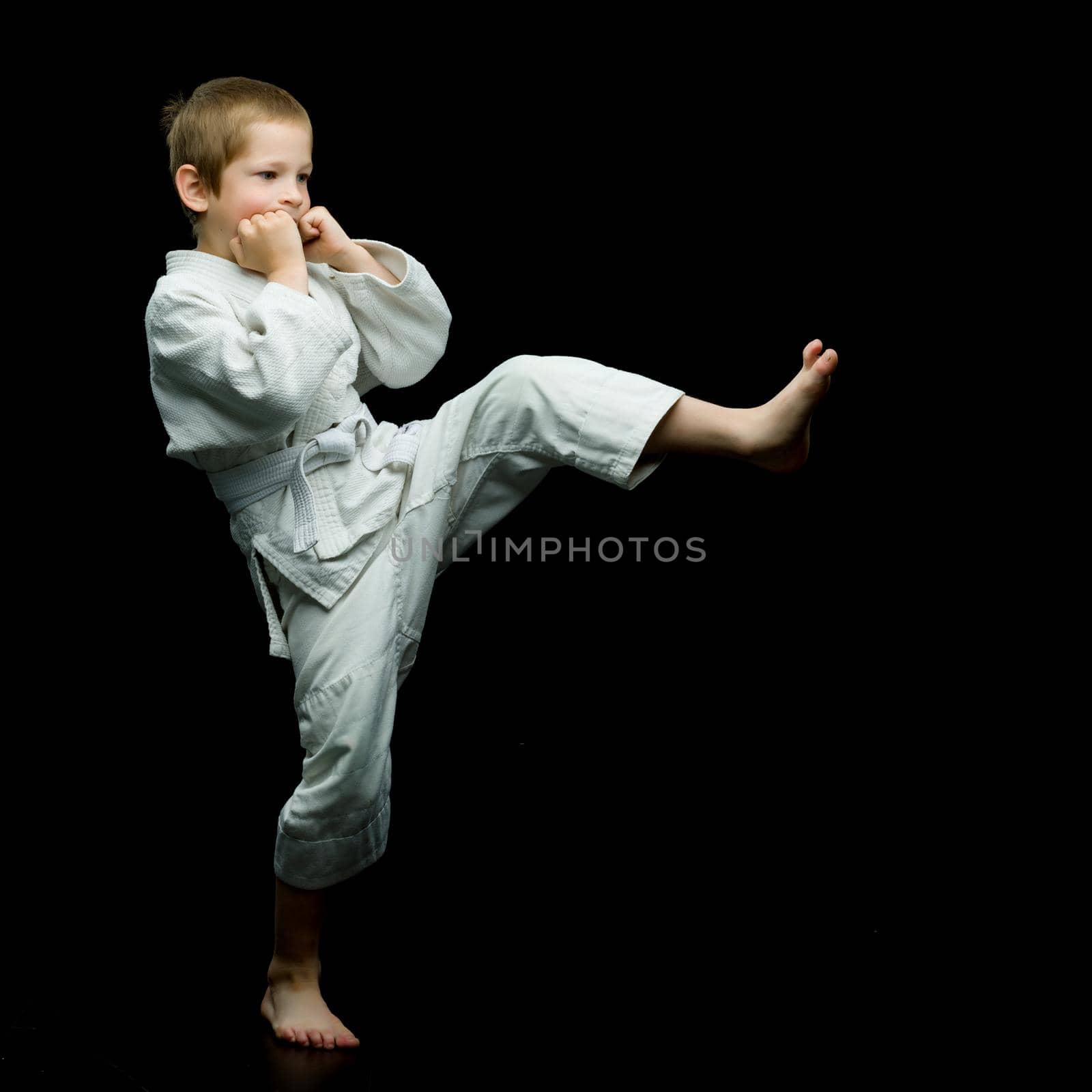 A boy in a white kimono working out blows in the studio . The concept of children's sports, karate, aikido