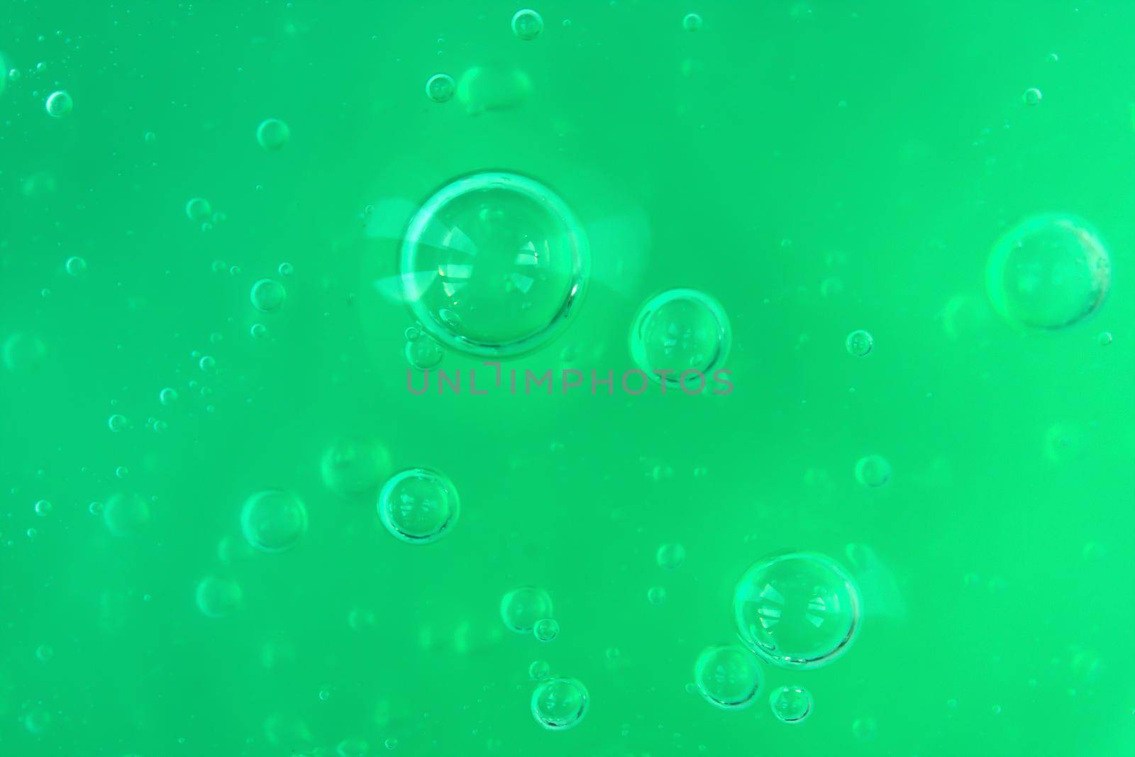 Texture of transparent green gel with air bubbles and waves on white background. Concept of skin moisturizing, body care and prevention of covid19. Liquid beauty product closeup. Backdrop, flat lay