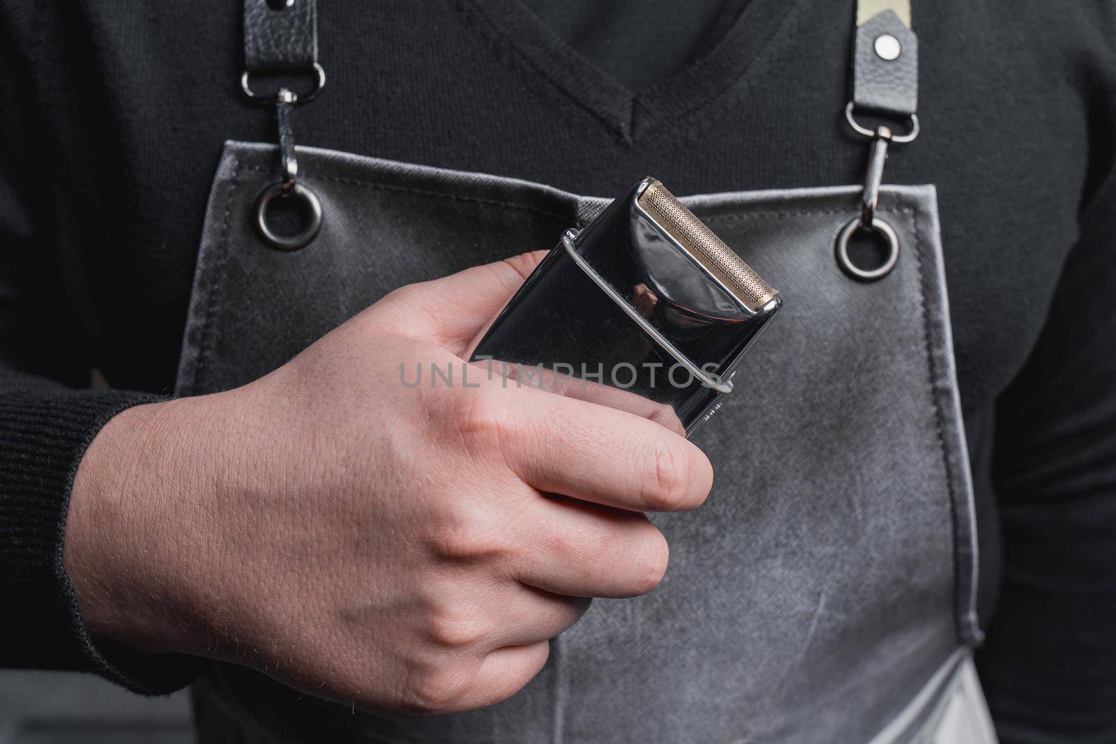 The hand of a barber or hairdresser holds an automatic clipper for cutting and shaving close-up against the background of the salon by AYDO8