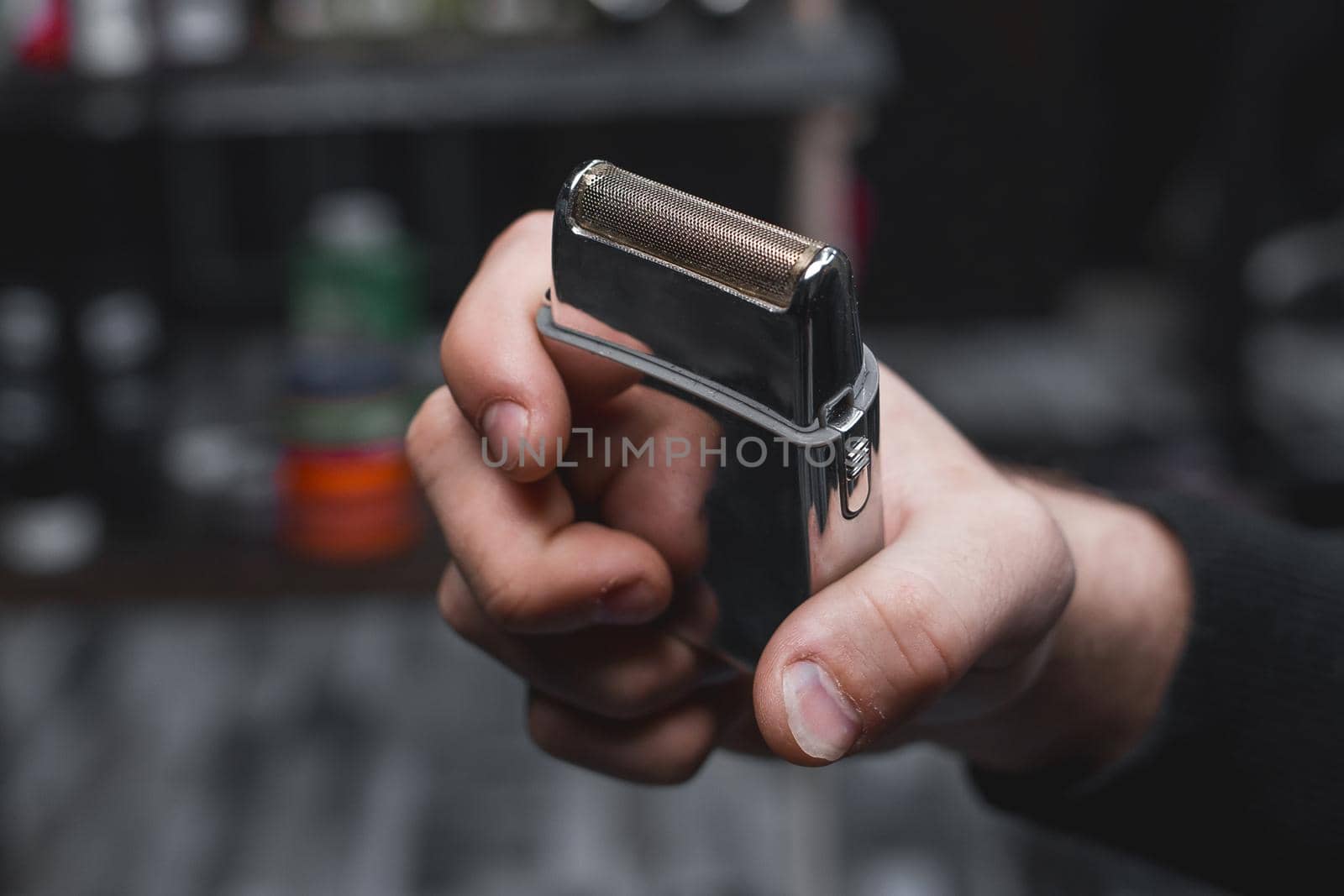 The hand of a barber or hairdresser holds an automatic clipper for cutting and shaving close-up against the background of the salon by AYDO8