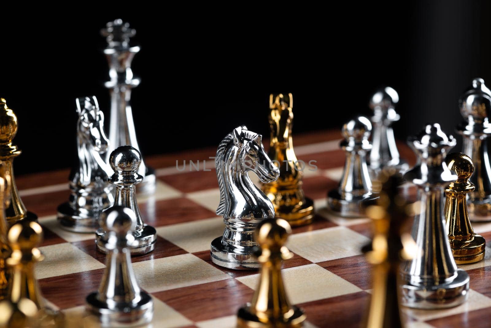 Gold and silver chess figures placed on wooden chessboard. Intellectual duel and tactical battle in business. Strategy planning, leadership and teamwork concept. Close-up metal chess pieces on board.