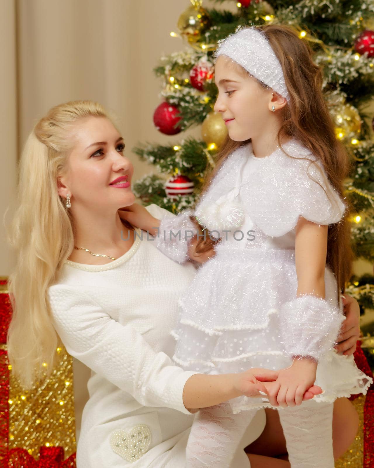 Happy young mother with her little daughter, on Christmas Eve near the Christmas tree with gifts and toys. The concept of holidays and happy childhood.