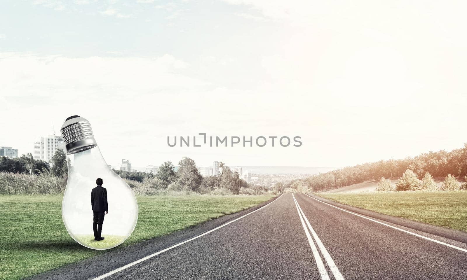 Young businessman trapped inside of light bulb on asphalt road