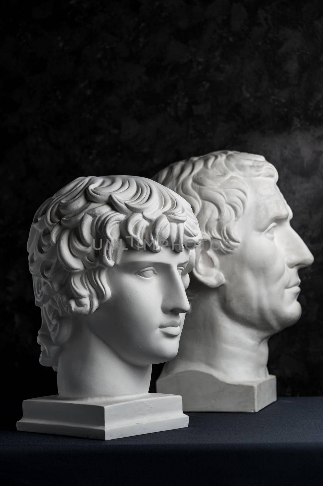 Gypsum copy of ancient statue Augustus and Antinous head on dark textured background. Plaster sculpture mans face. by bashta