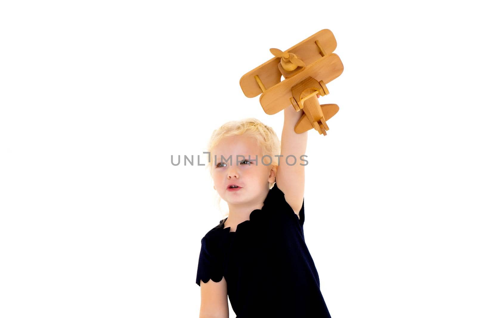 Happy little girl is playing with a wooden plane in the studio on a white background. The concept of emotions and children's games. Isolated.
