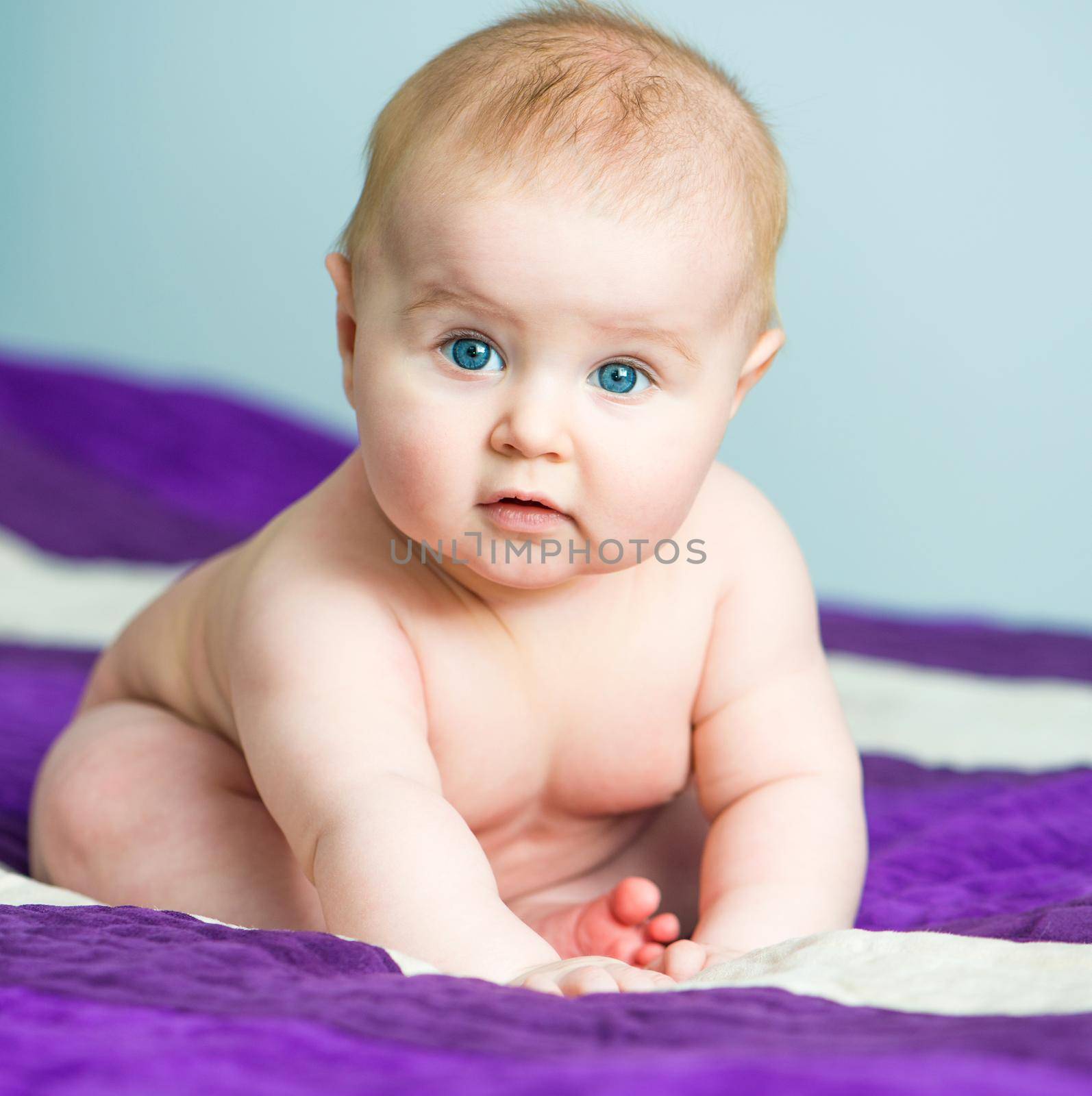 blue-eyed baby sitting on the bed