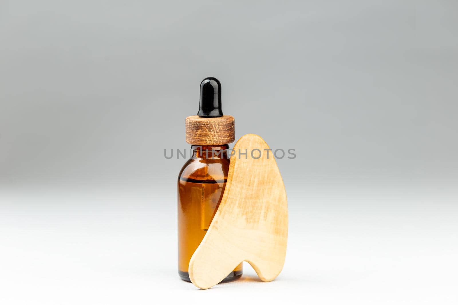 Oil bottle and gua sha wooden scraper massager tool at gray background. Beauty treatment concept. Copy text for text