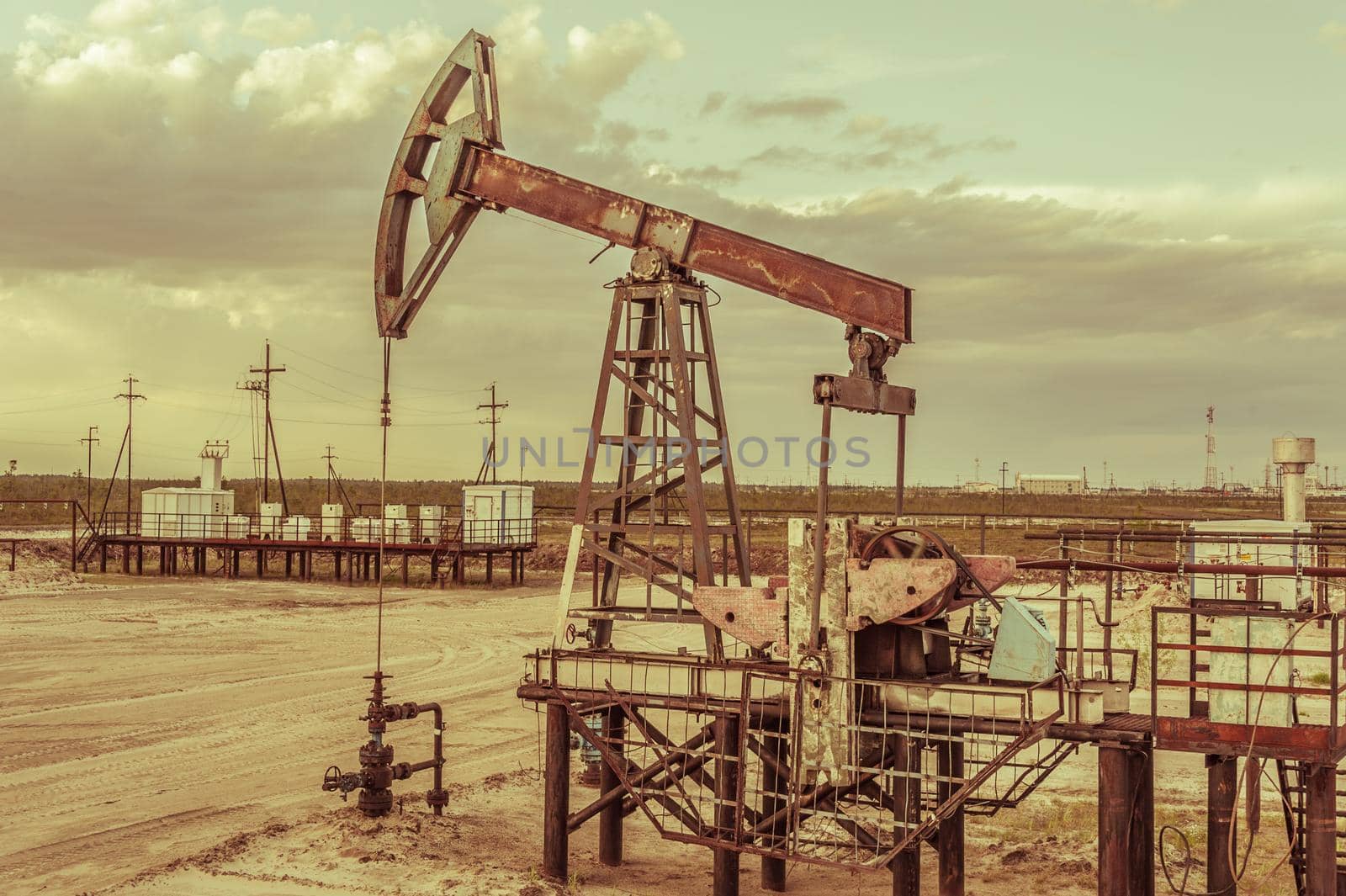 Oil pump jack on a oil field. Cloudy sky background. Extraction of oil. Petroleum concept. Toned.