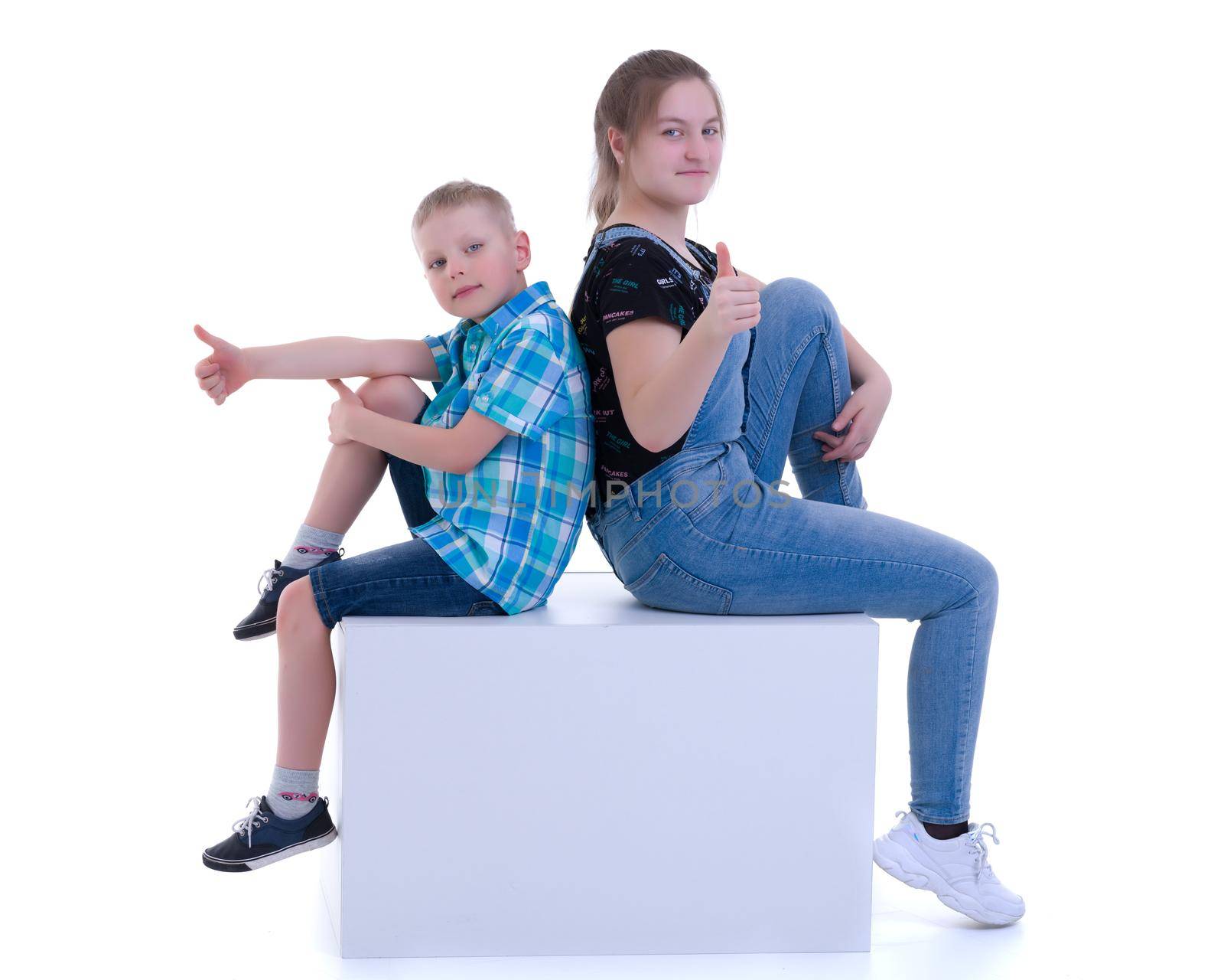 A boy and a girl, brother and sister are photographed in a studio on a white cube. Isolated on white background