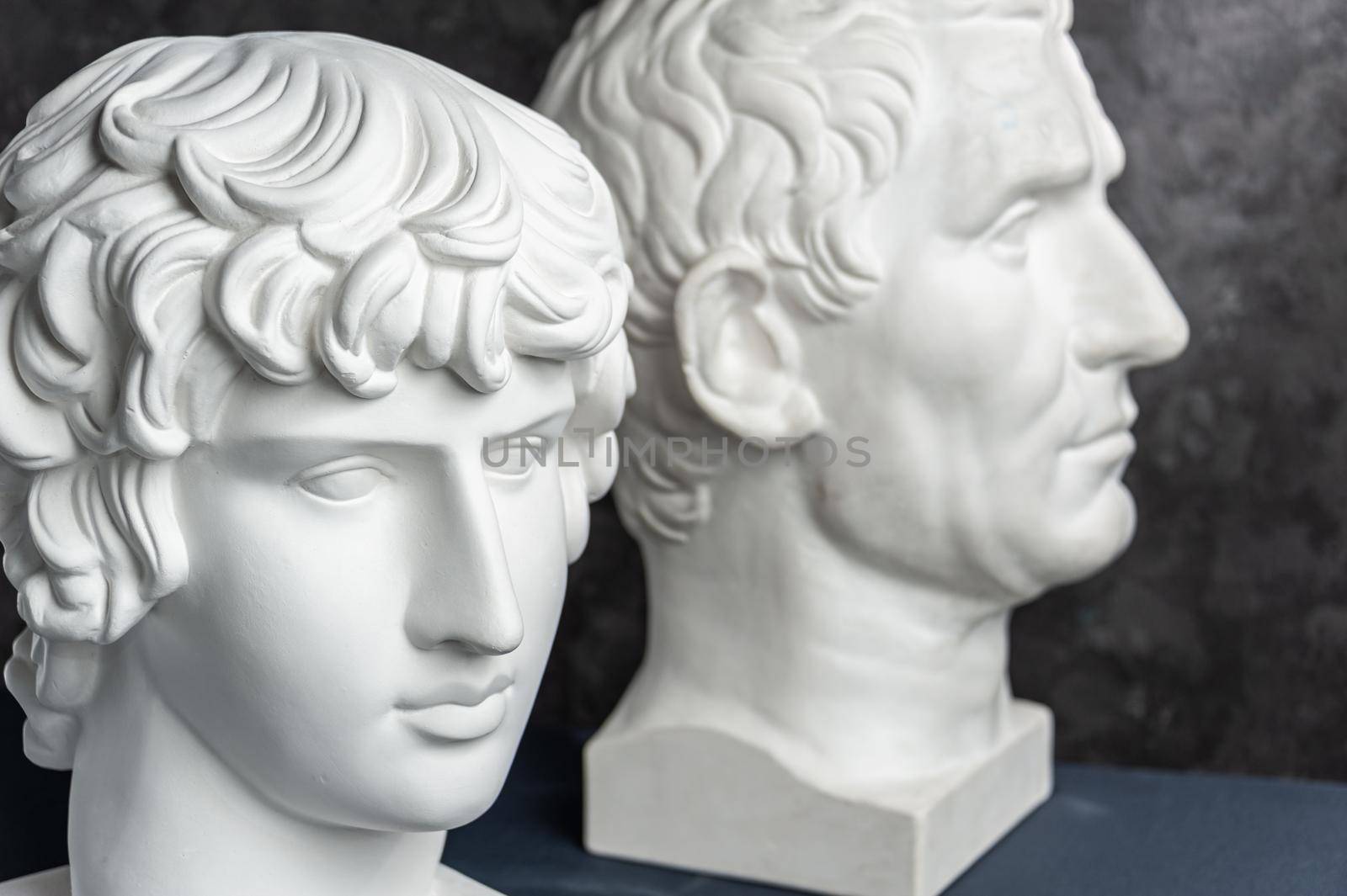 Group gypsum busts of ancient statues human heads for artists on a dark background. Plaster sculptures of antique people faces. Renaissance epoch style. Blank for creativity. Academic subject.