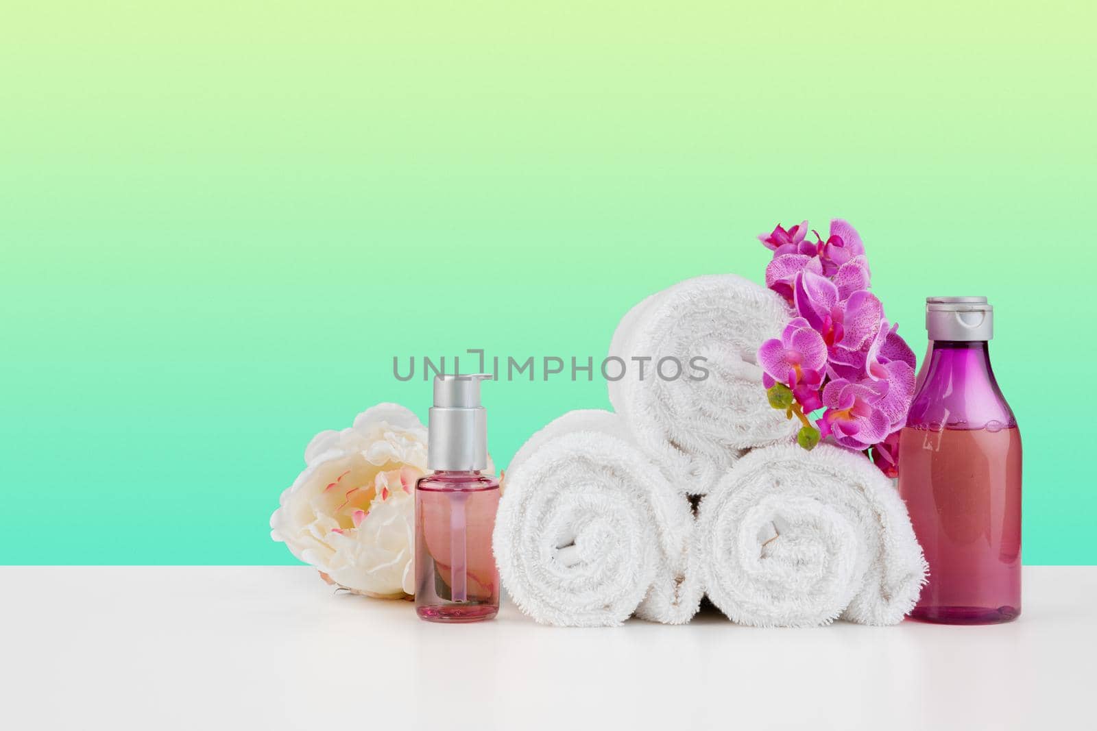 Stack of white towels and bottles of skincare on white table, front view