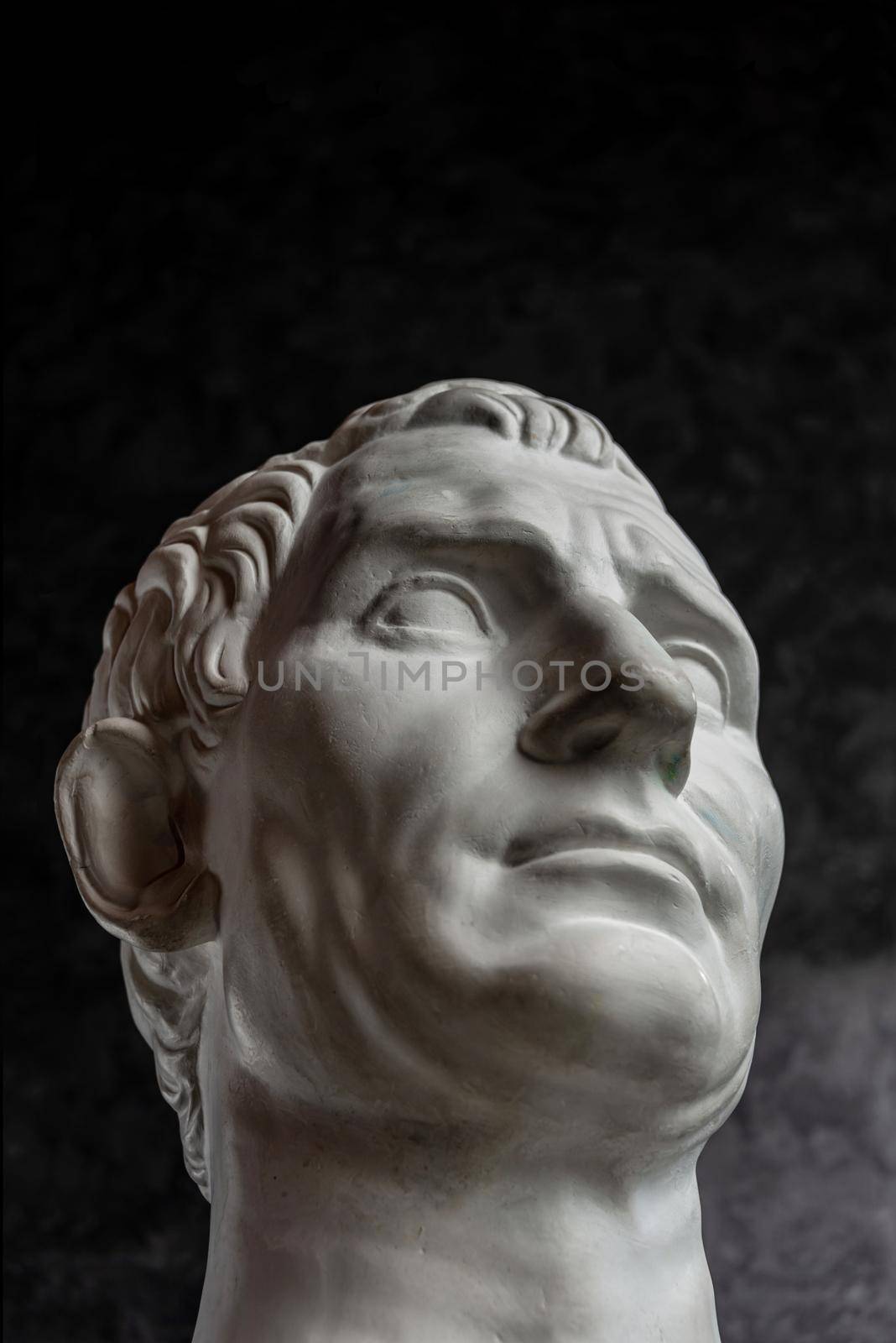 White gypsum copy of ancient statue of Guy Julius Caesar Octavian Augustus head for artists on a dark textured background. Plaster sculpture of man face.