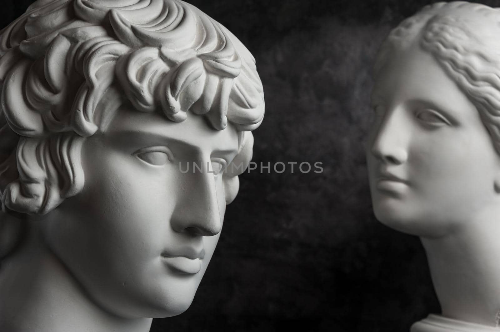 White gypsum copy of ancient statue of Antinous and Venus head for artists on a dark textured background. Plaster sculpture of statue face.