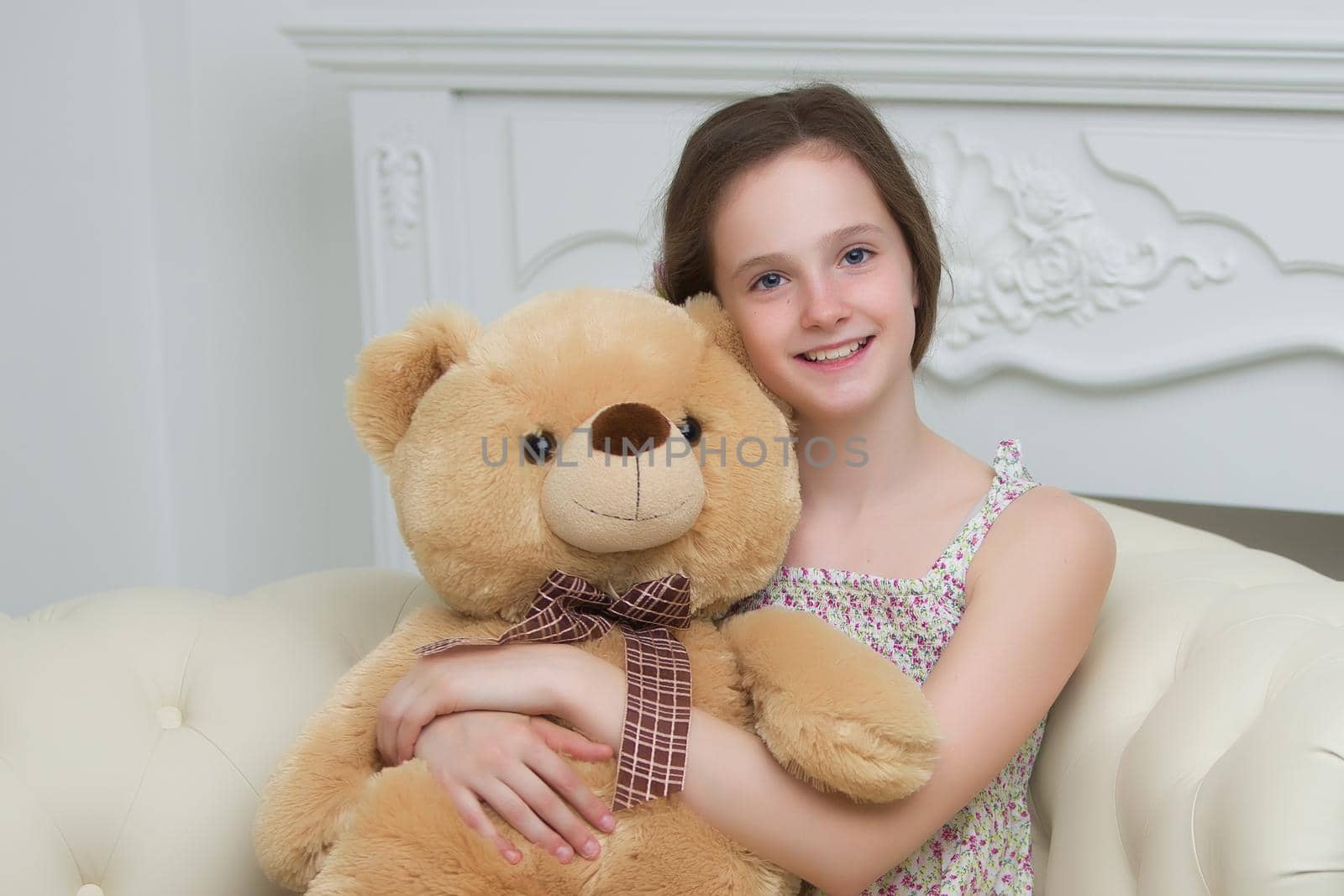 A teenage girl of school age is sitting on the couch with a big teddy bear. The concept of a happy childhood.