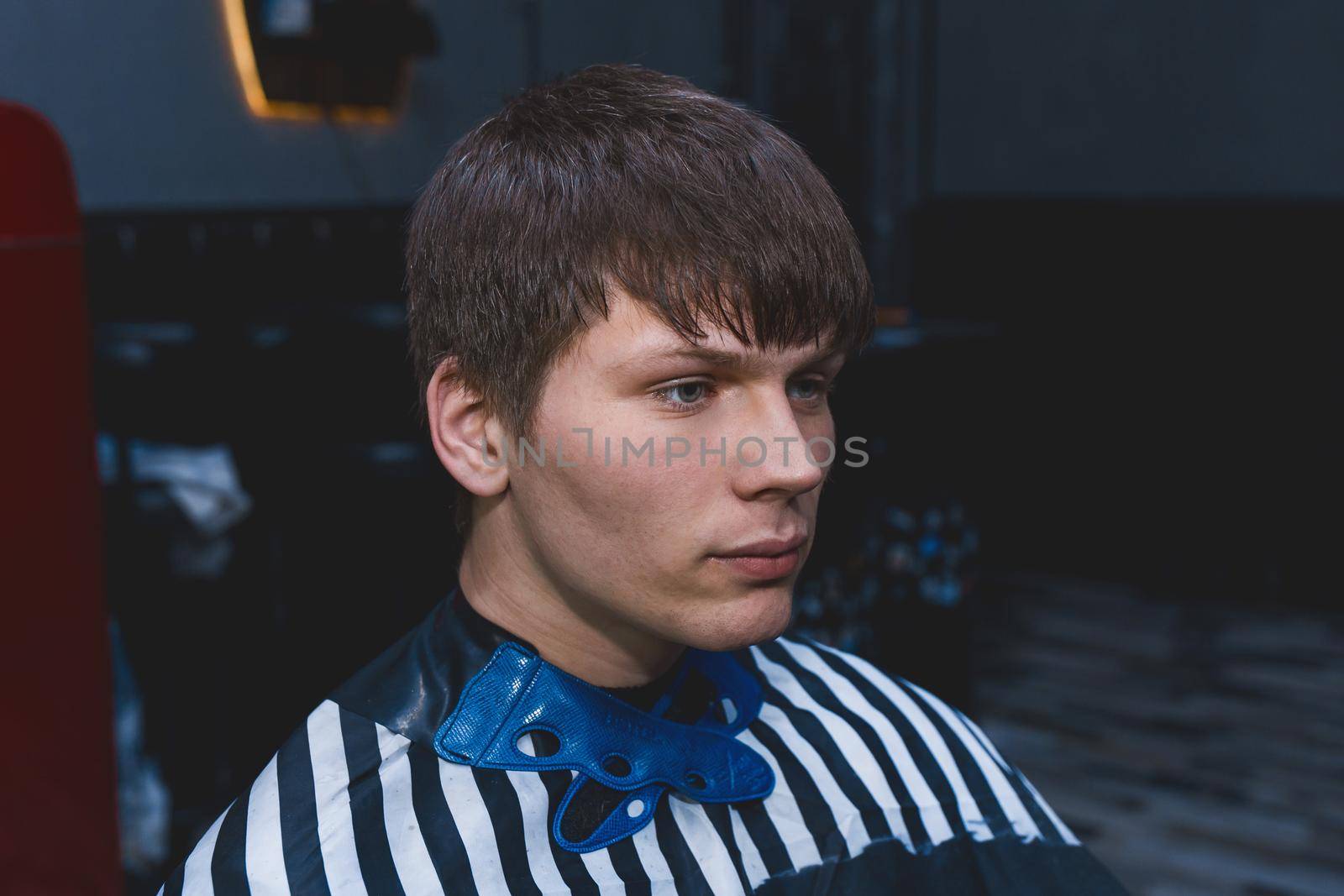 A shaggy untrimmed guy of Caucasian appearance with dark long hair sits in a chair in a hairdresser's client for a haircut. The need for hairdressing services, hair care.