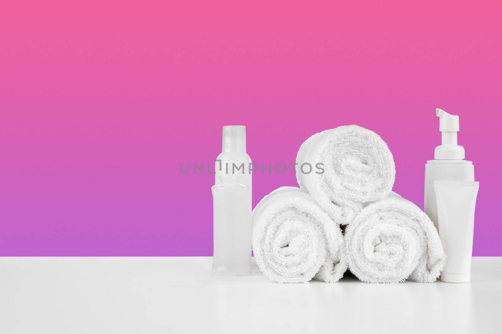 Pile of towels, bottles with shampoo on white table isolated