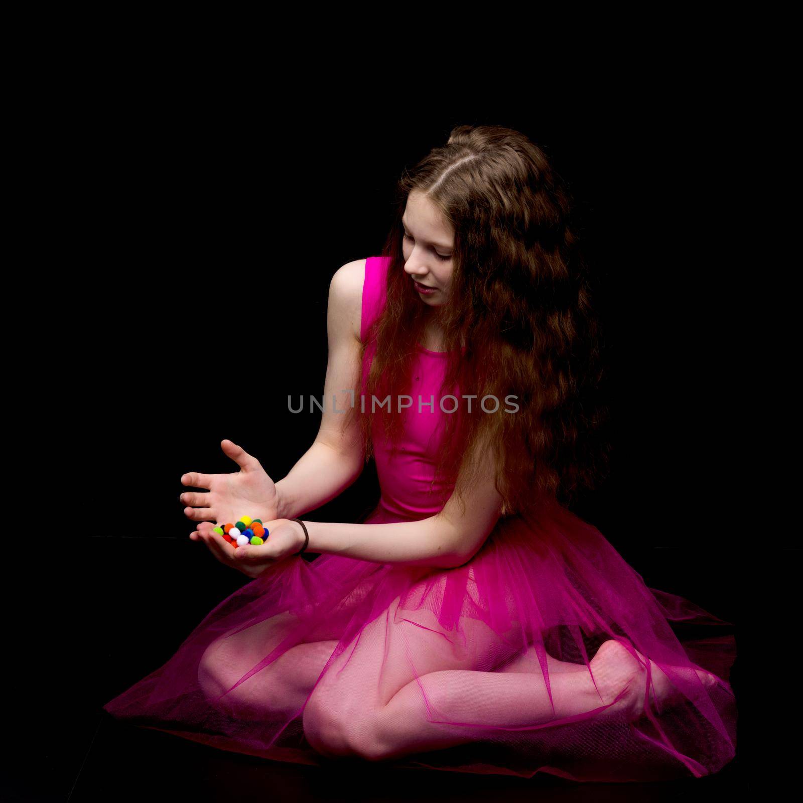 A beautiful little gymnast girl of school age holds multicolored confetti in her palms. Studio photography on a black background.