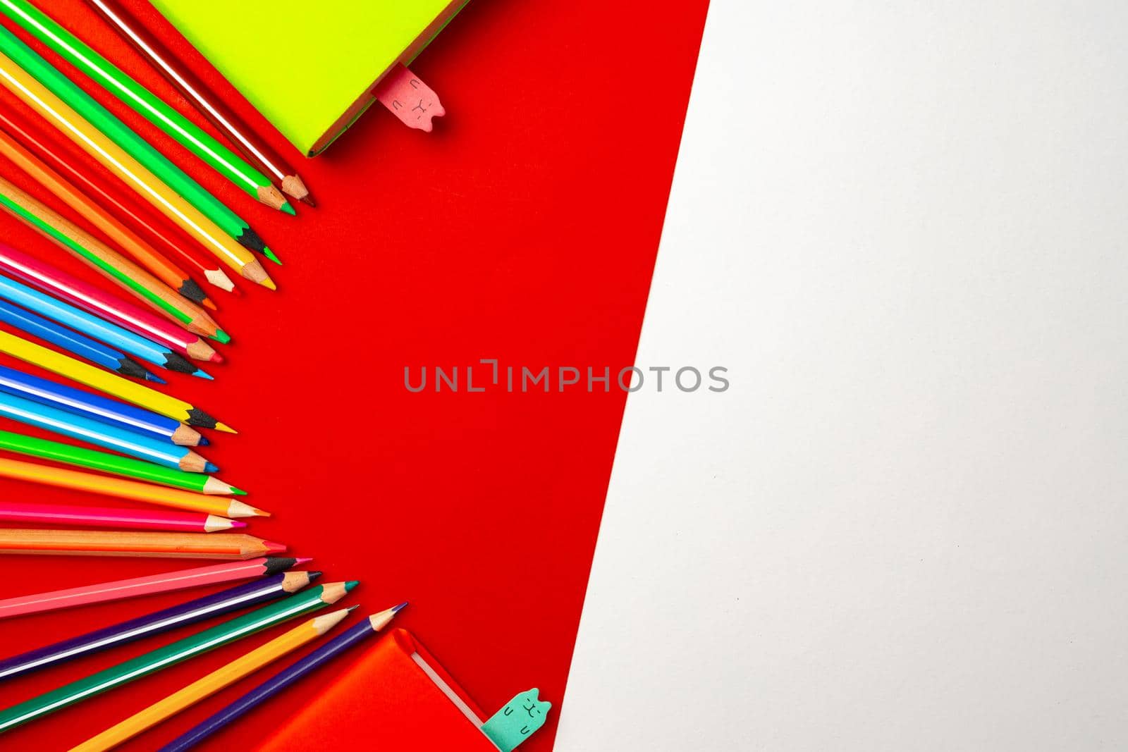 Colorful pencils and notepads on paper background top view, copy space