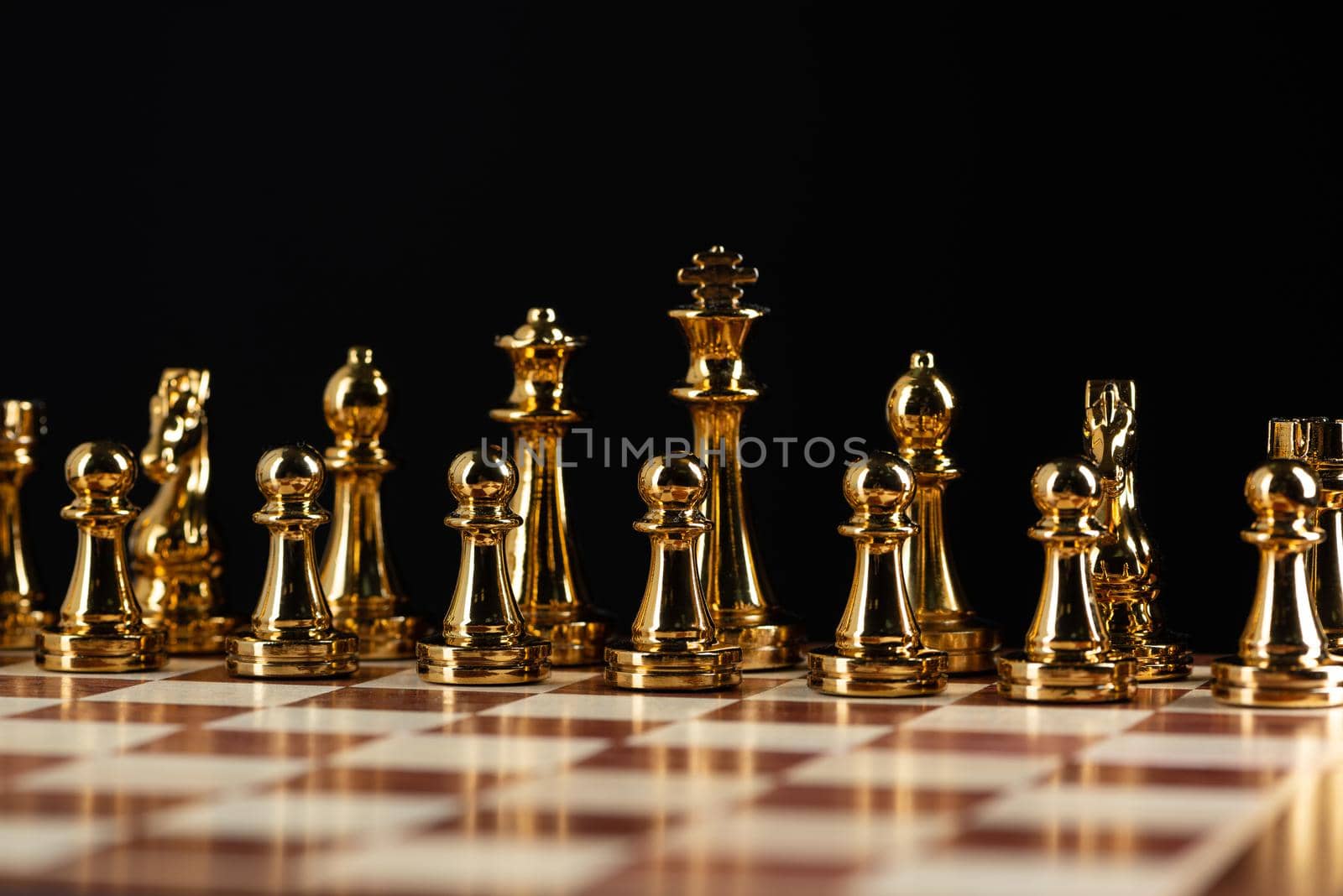 Golden chess figures standing on chessboard. Intellectual competition and fight in business. Strategy planning and leadership concept with copy space. Gold chess pieces in row on black background.