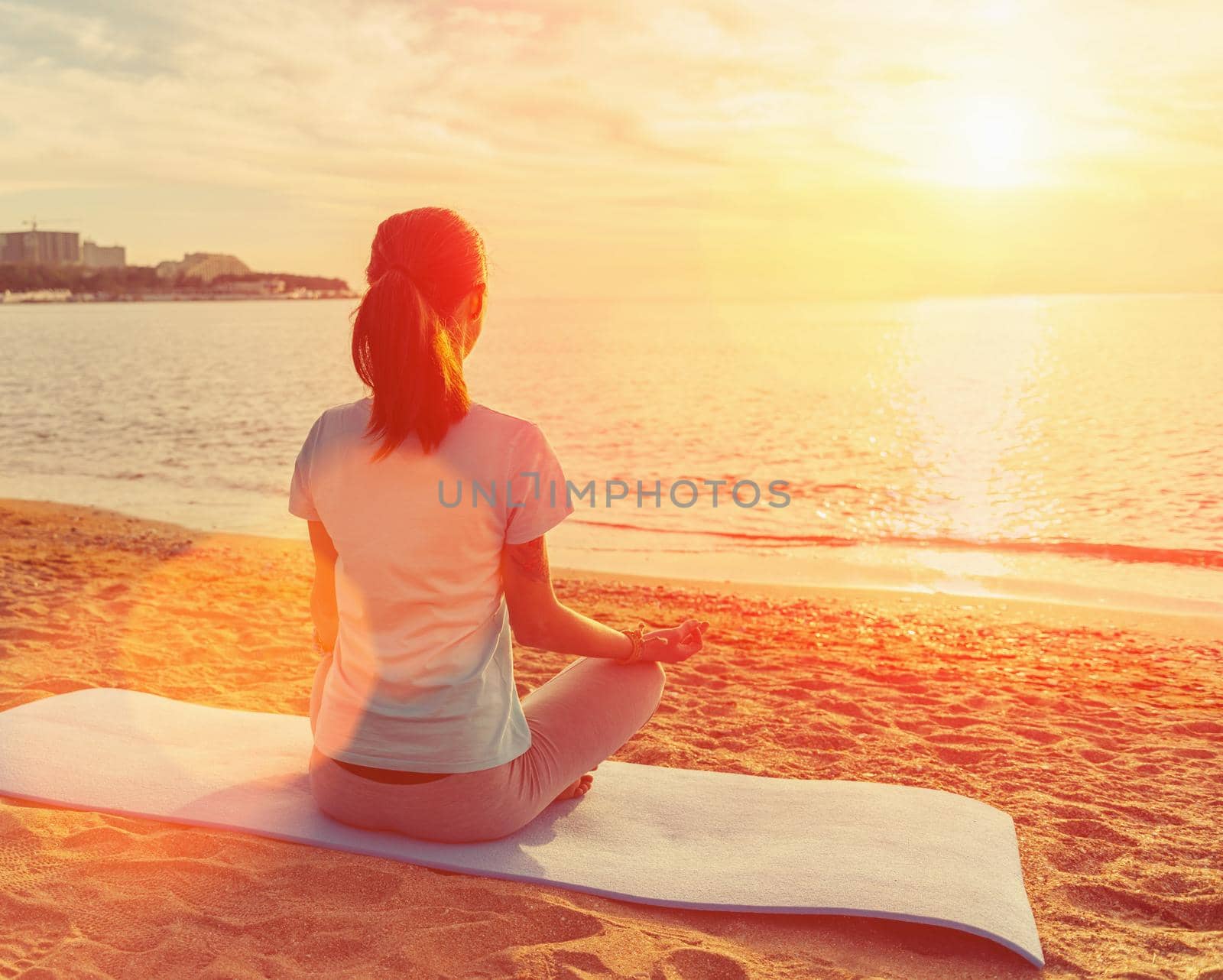 Woman meditating in pose of lotus at sunset by alexAleksei