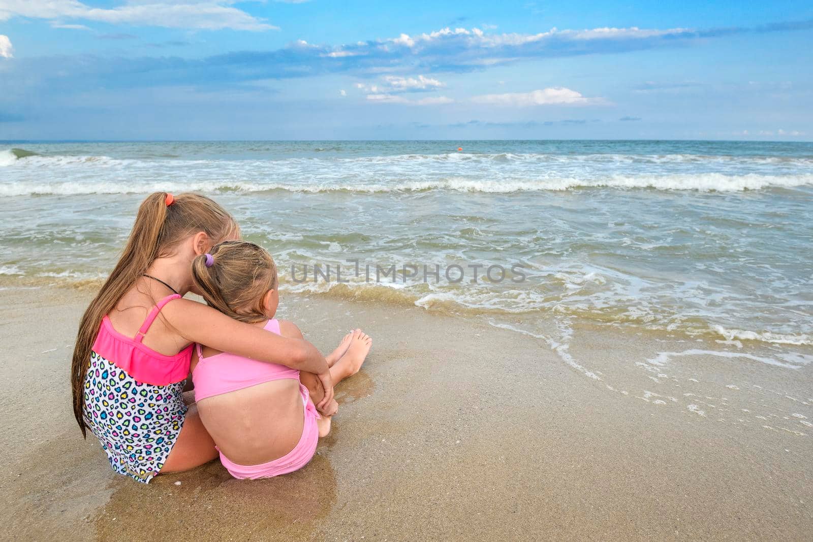 Two girls sitting on the beach and looking at the sea. Children on the sea beach and beautiful skyline. by esvetleishaya