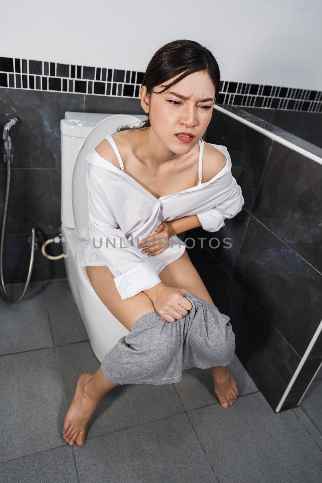 woman sitting on toilet in the bathroom and holding her painful Stomach