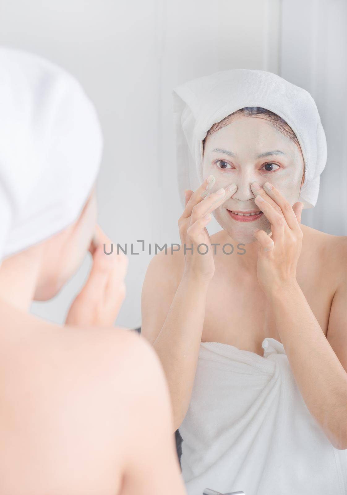 woman applying mask on her face and looking in the mirror in the bathroom