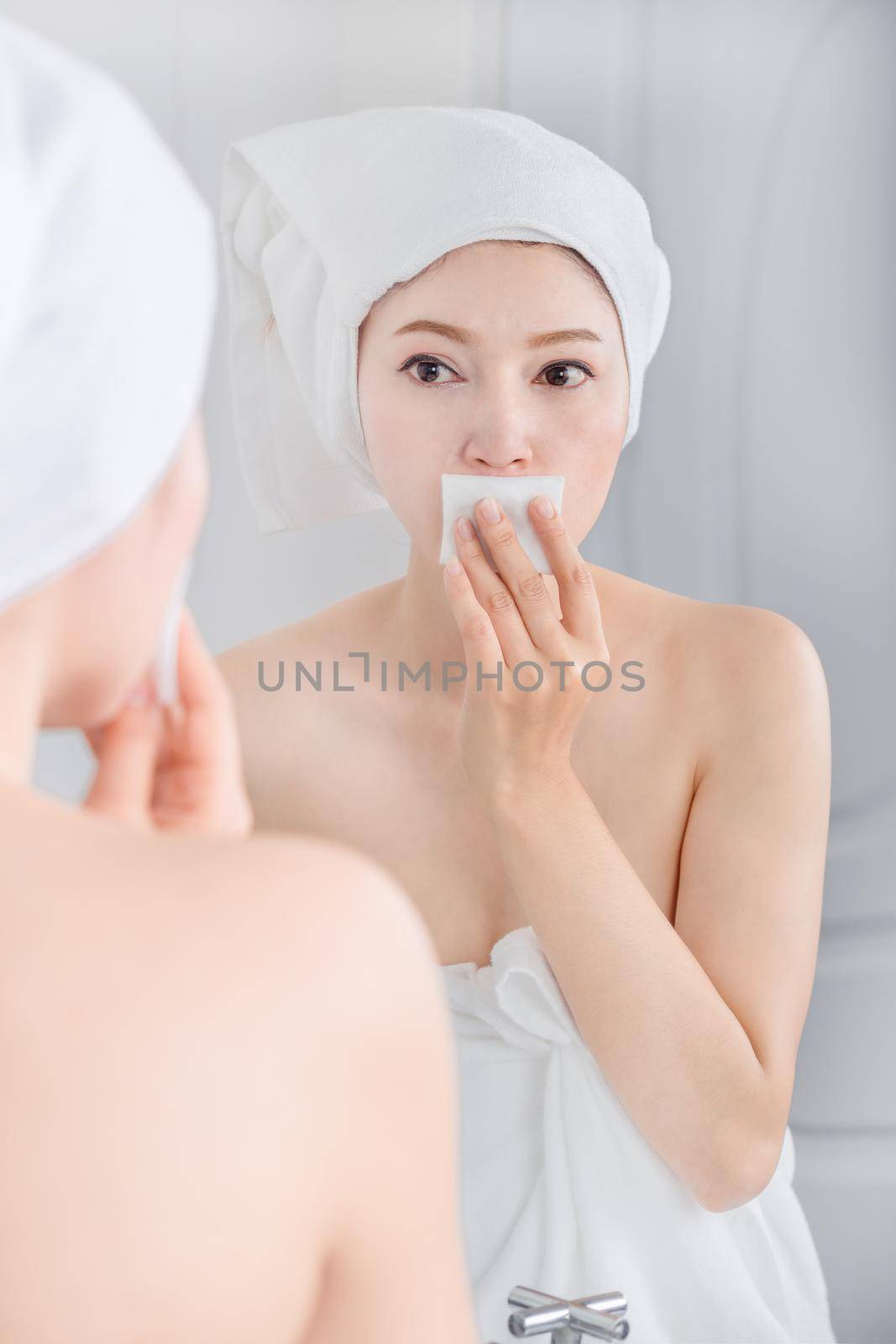 Beautiful woman looking mirror and cleaning her face with cotton