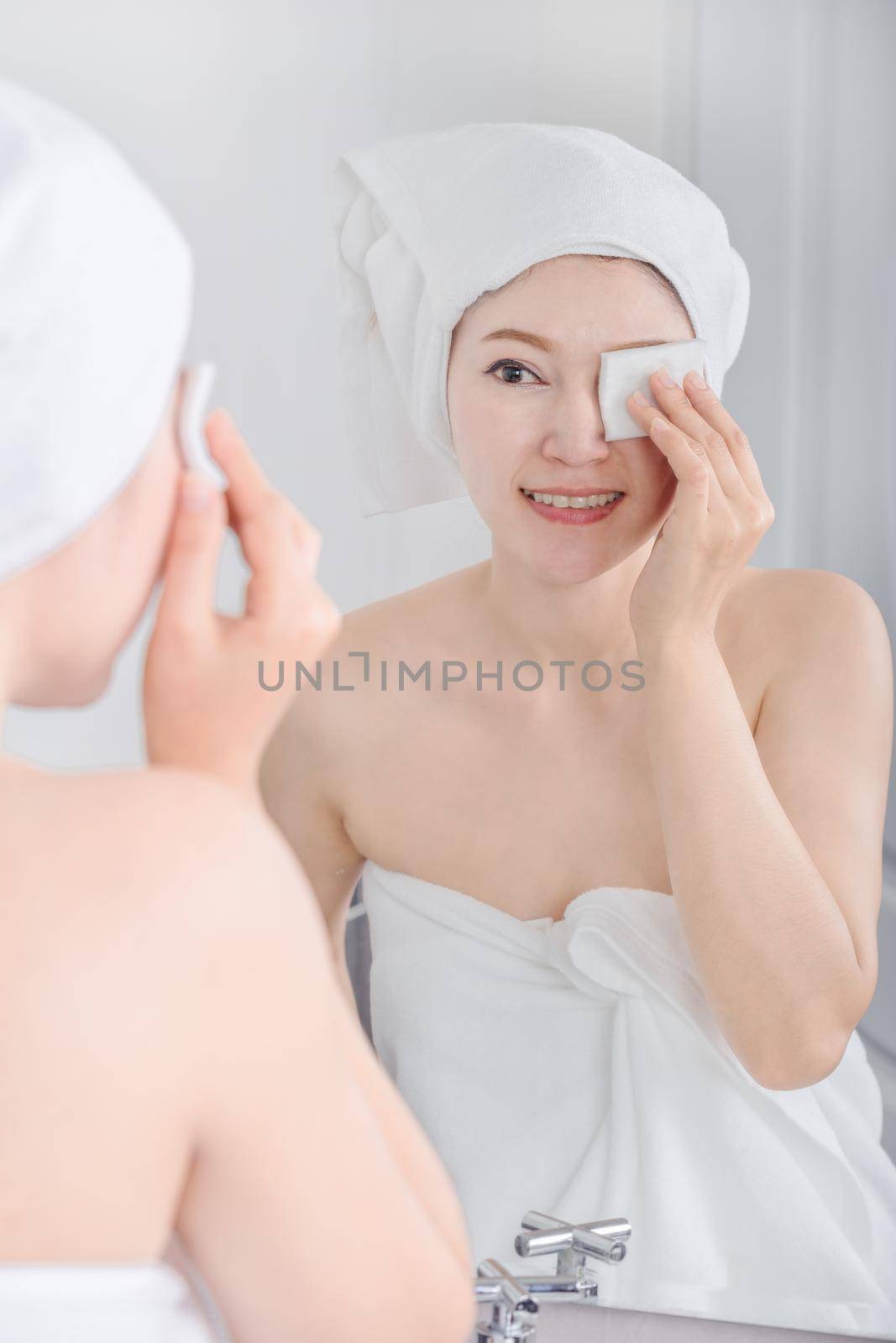 Beautiful woman looking mirror and cleaning her face with cotton