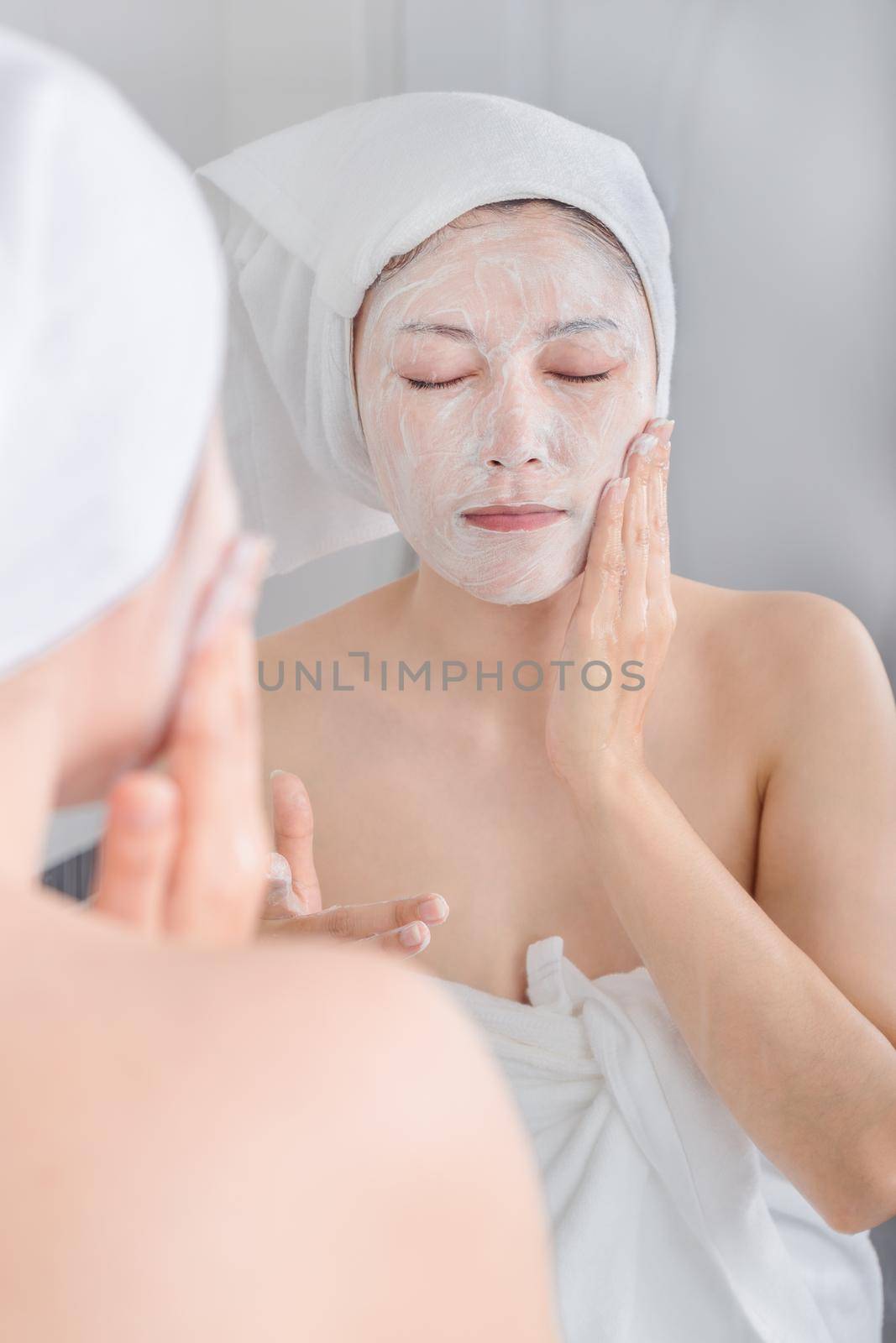 woman applying mask on her face and looking in the mirror in the bathroom