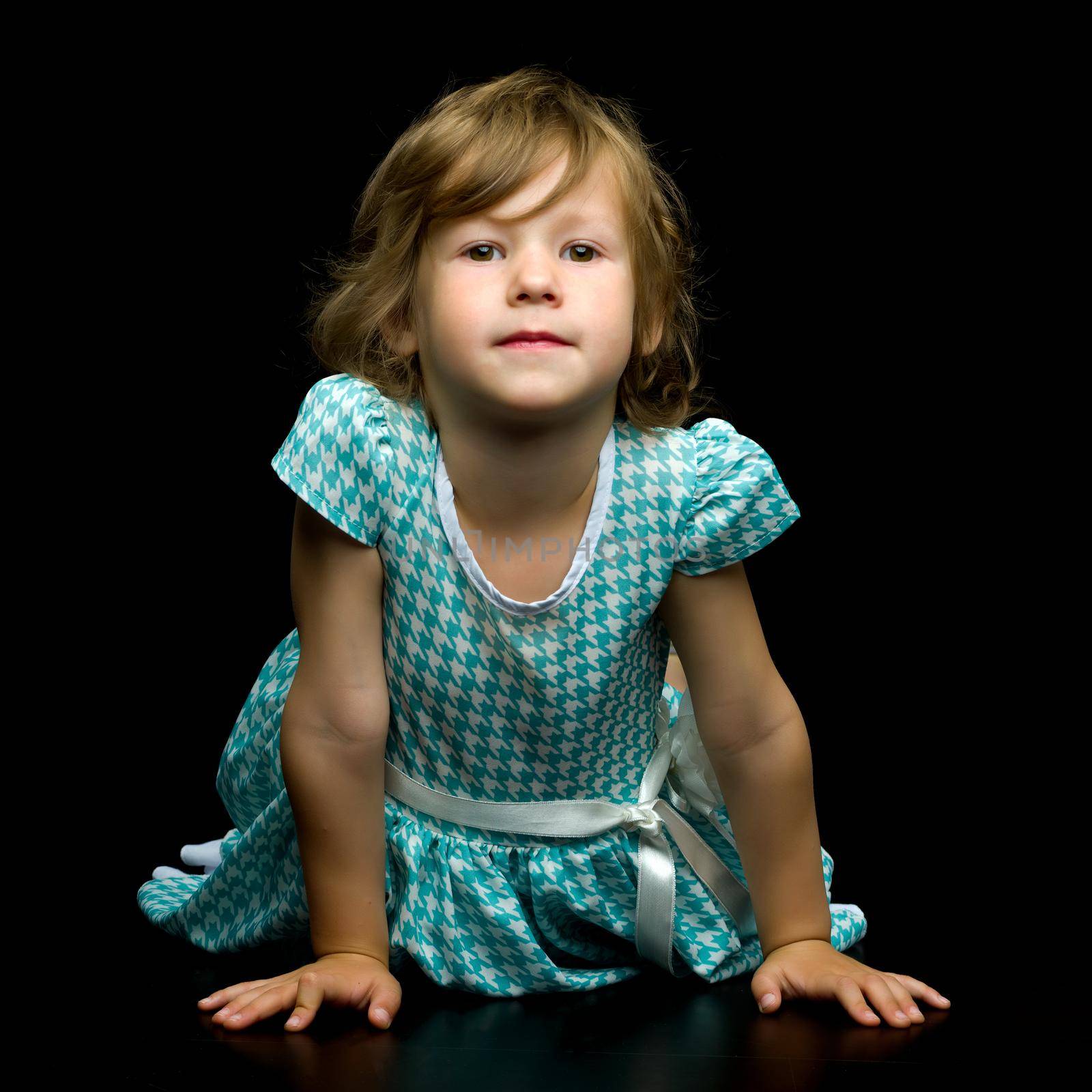 Charming little girl is lying on the studio floor on a black background. Concept for happy childhood, style and fashion