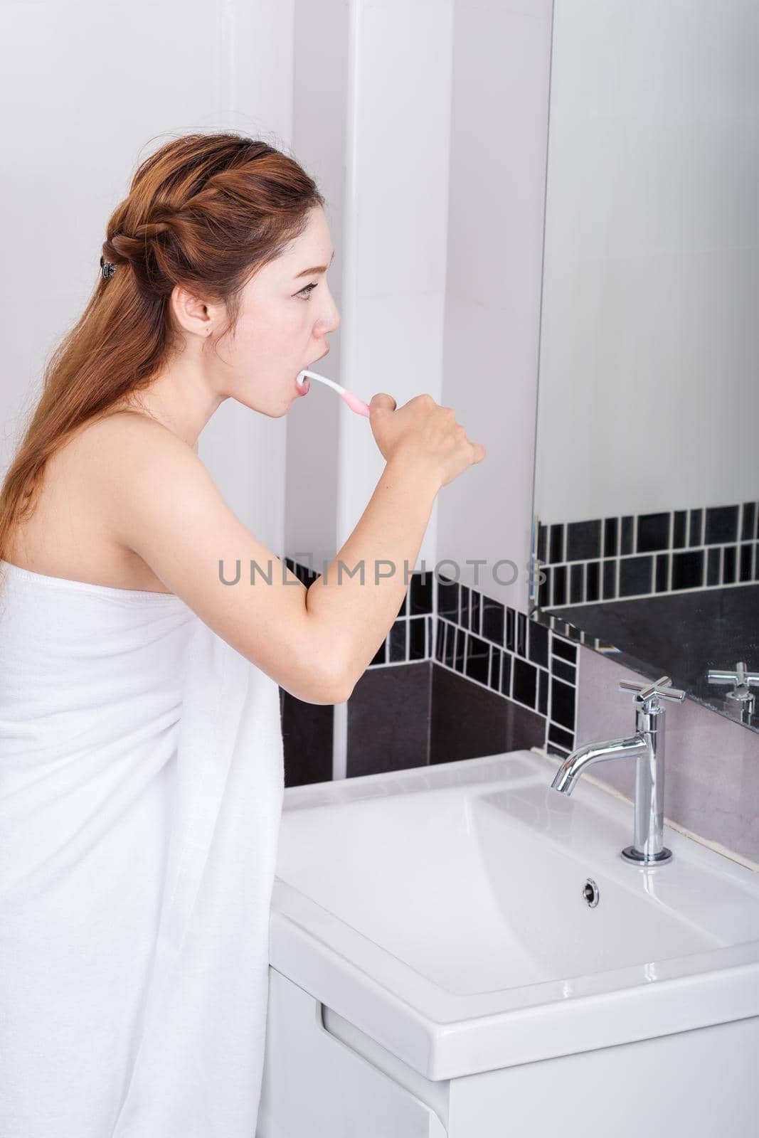 woman in bath towel brushing teeth with mirror in bathroom by geargodz