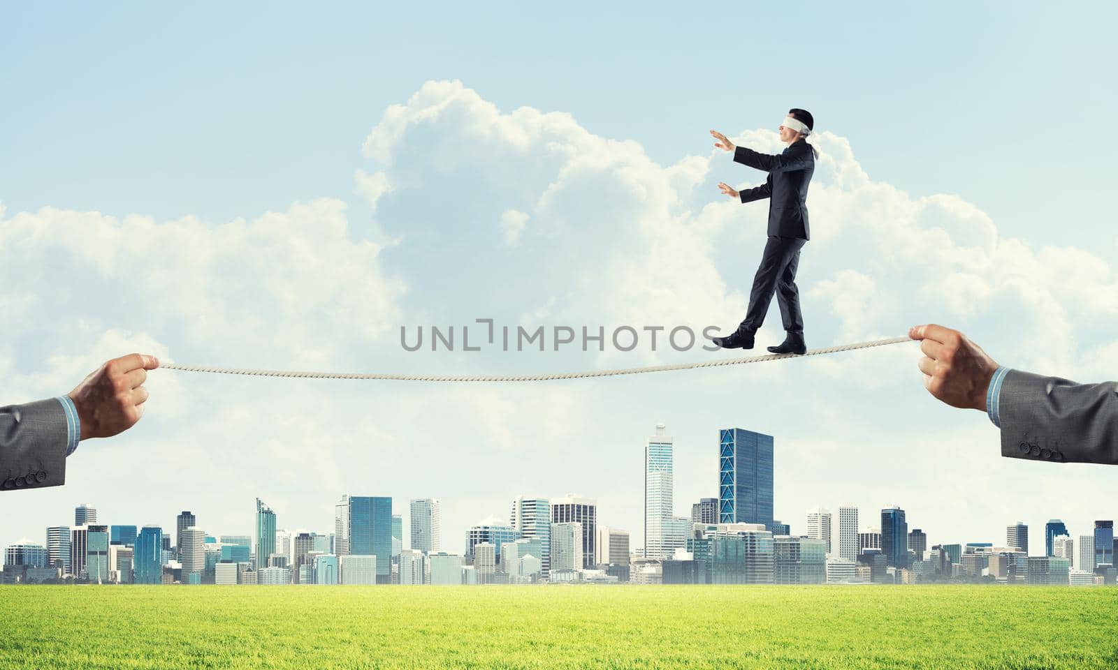 Businessman with blindfolder on eyes walking on rope over cityscape background