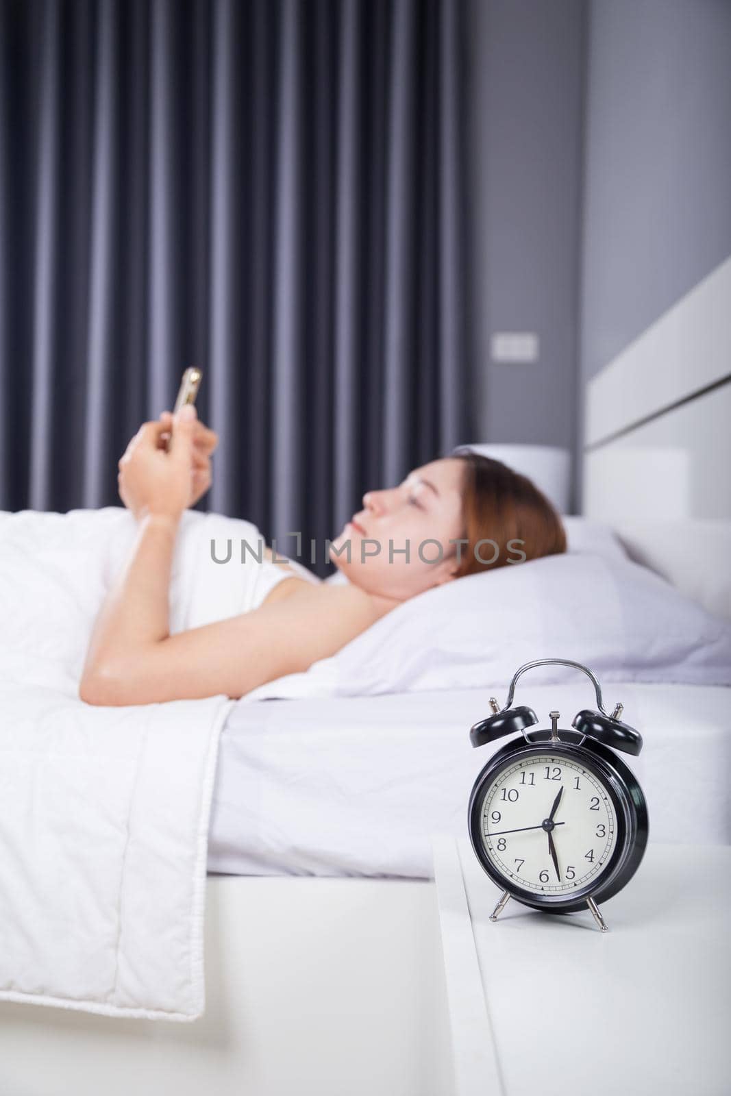 clock with woman using her smartphone on bed in the bedroom 