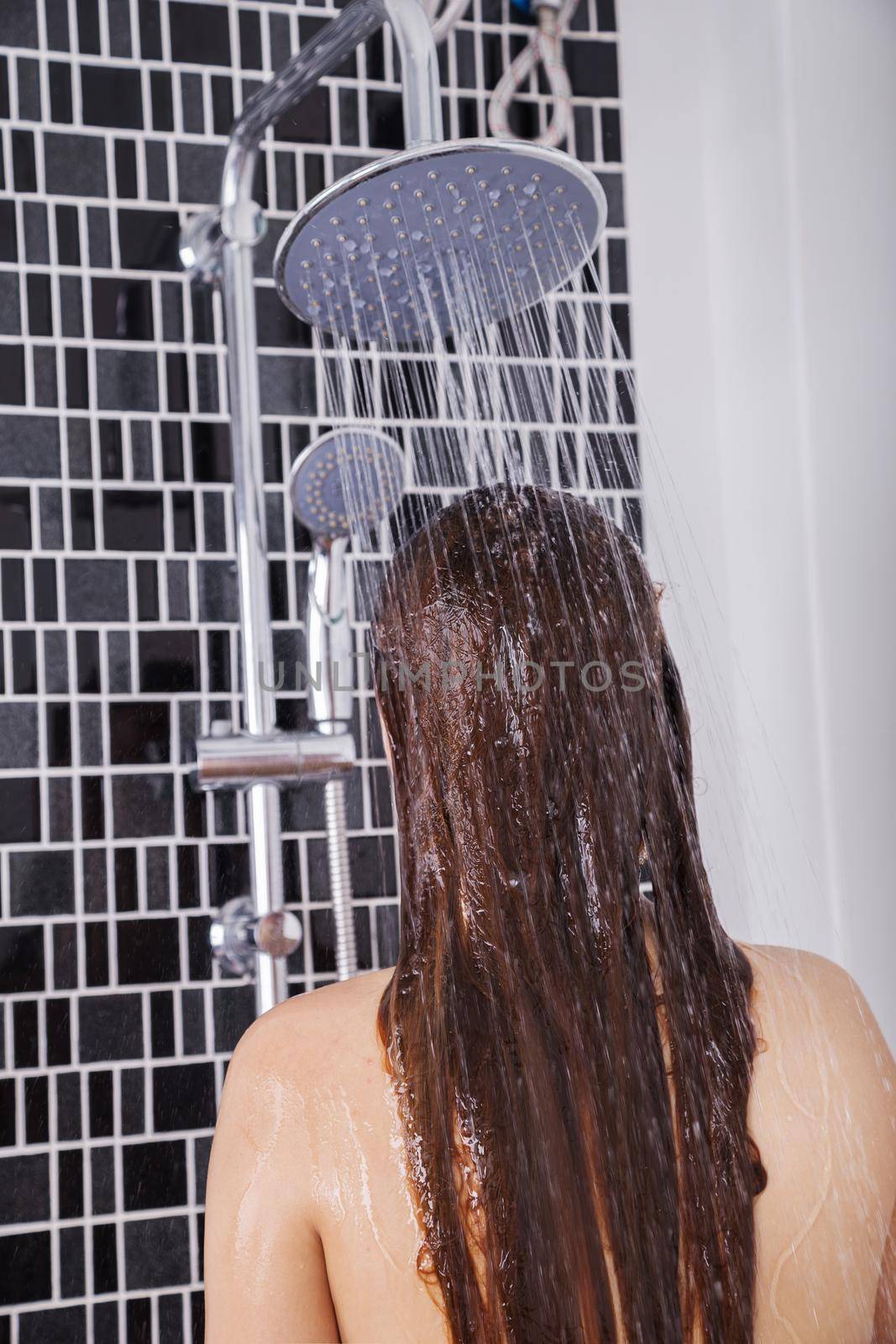 woman is washing her hair and face by rain shower head, rear view