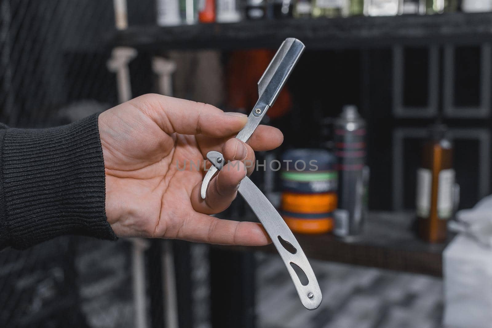 The hand of a barber or professional hairdresser holds a straight tool sharp razor equipment for shaving and beard care, close-up by AYDO8