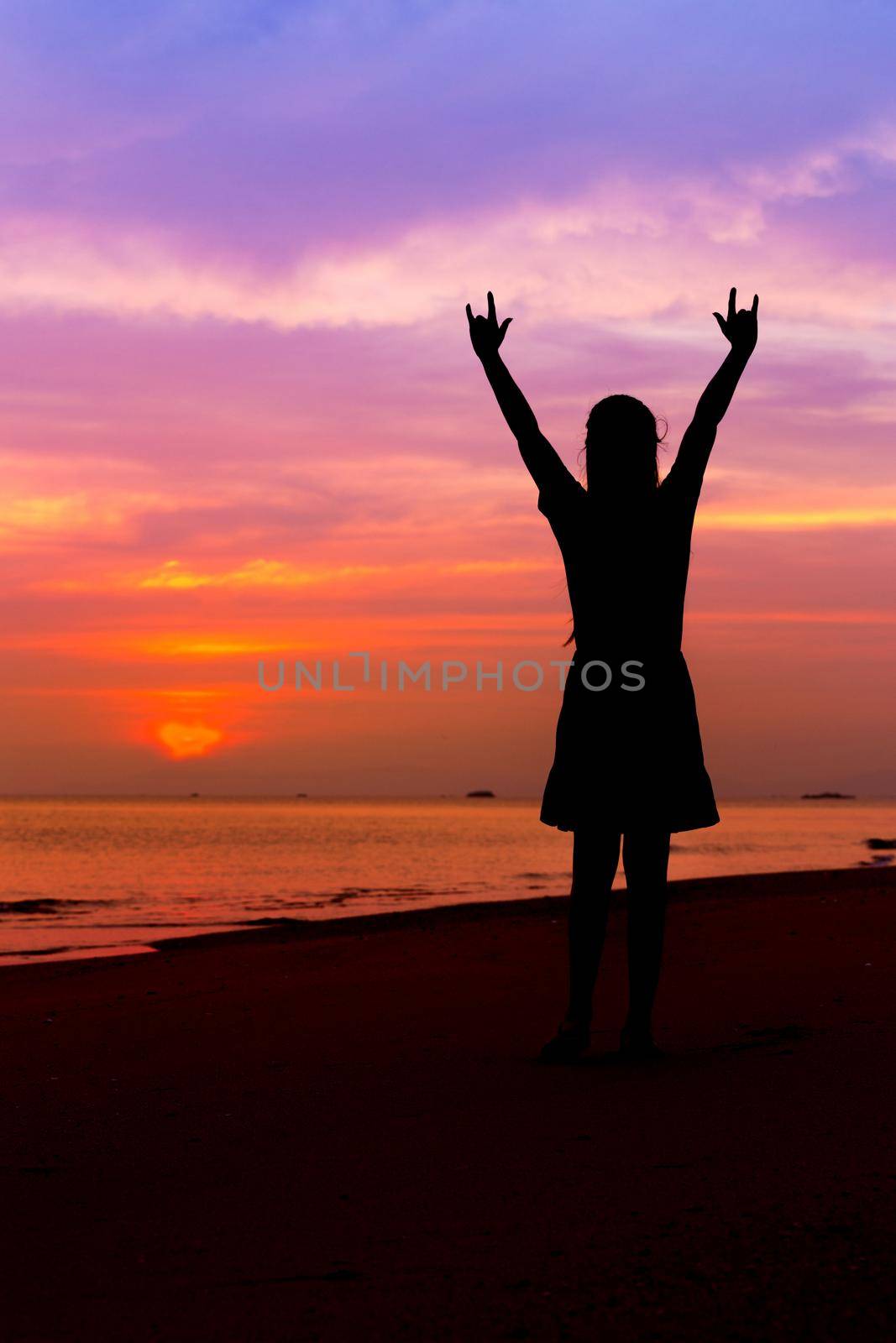 Silhouette of woman with hands up and showing I LOVE YOU sign on sea beach at sunset by geargodz
