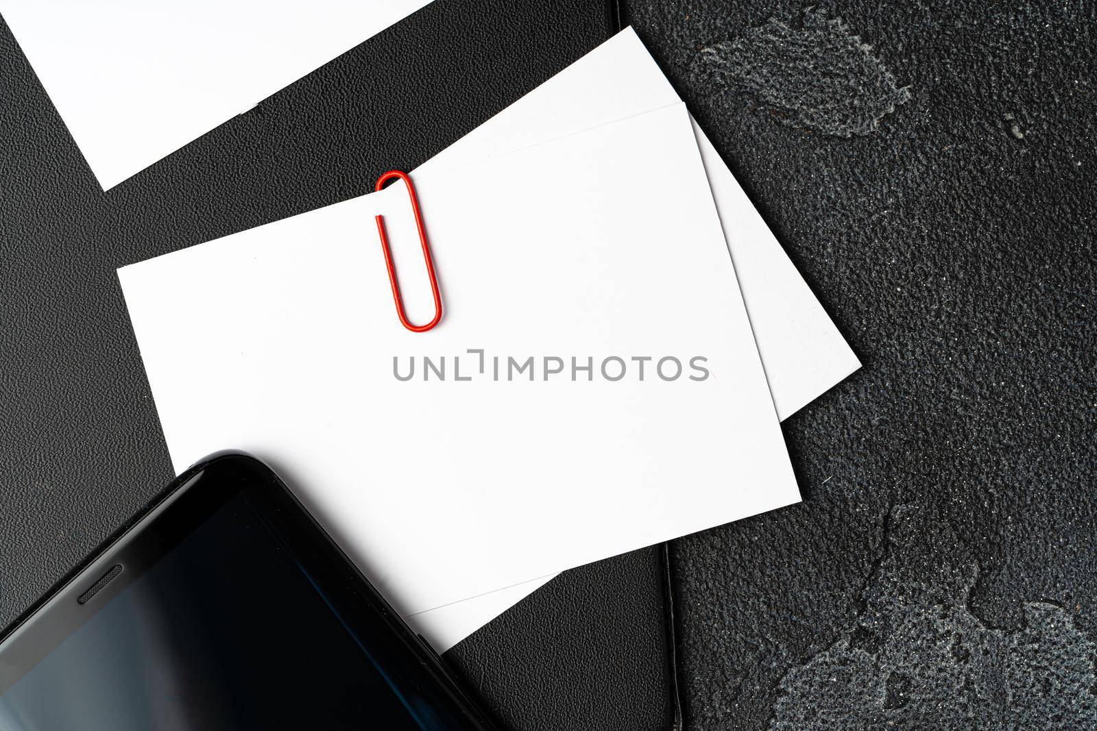 White businesscards united with a paper clip on a black rough background, copy space