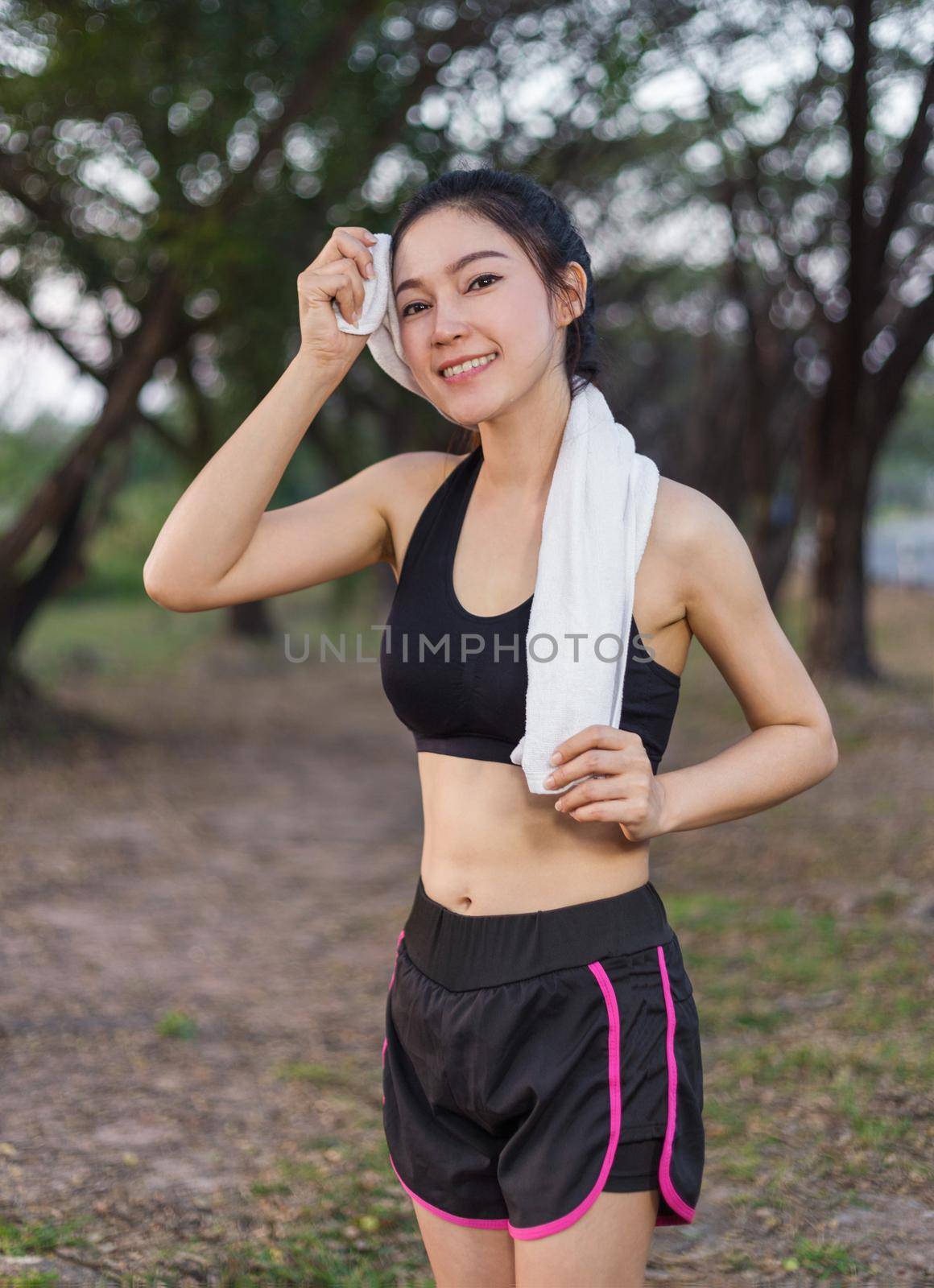 young sporty woman resting and wiping her sweat with a towel after workout sport exercises outdoors at the park