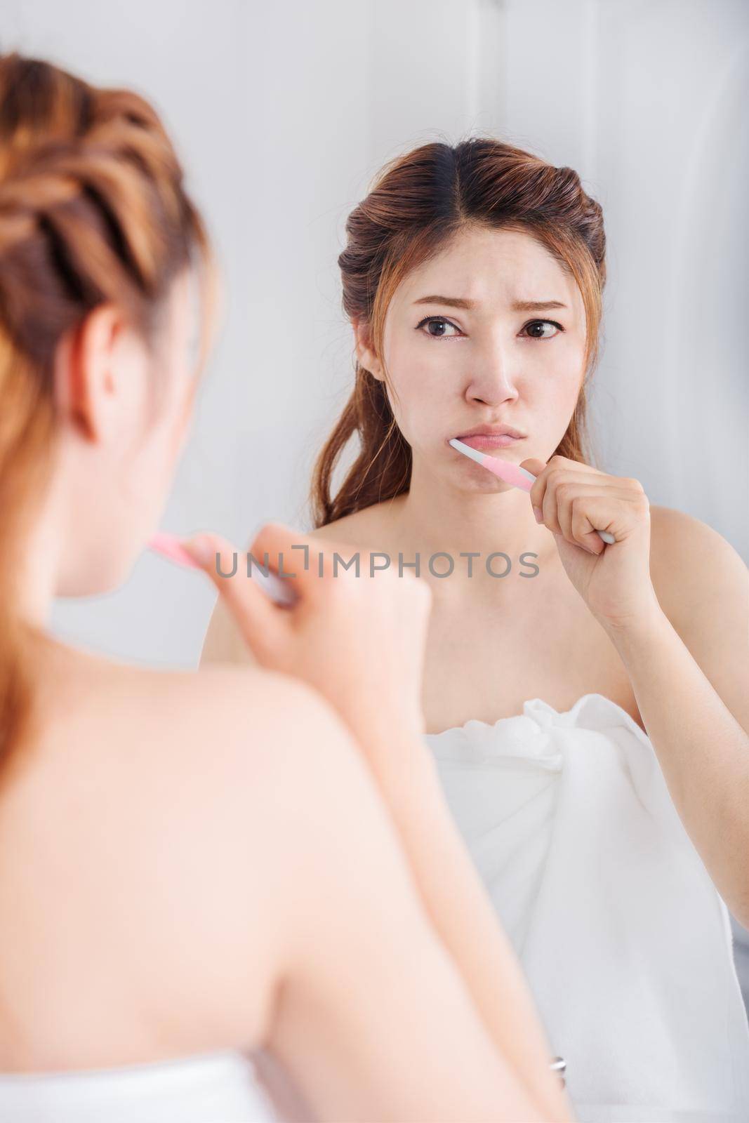 unhappy woman in bath towel brushing teeth with mirror in the bathroom
