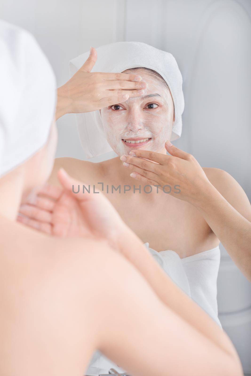 woman applying mask on her face and looking in the mirror in the bathroom