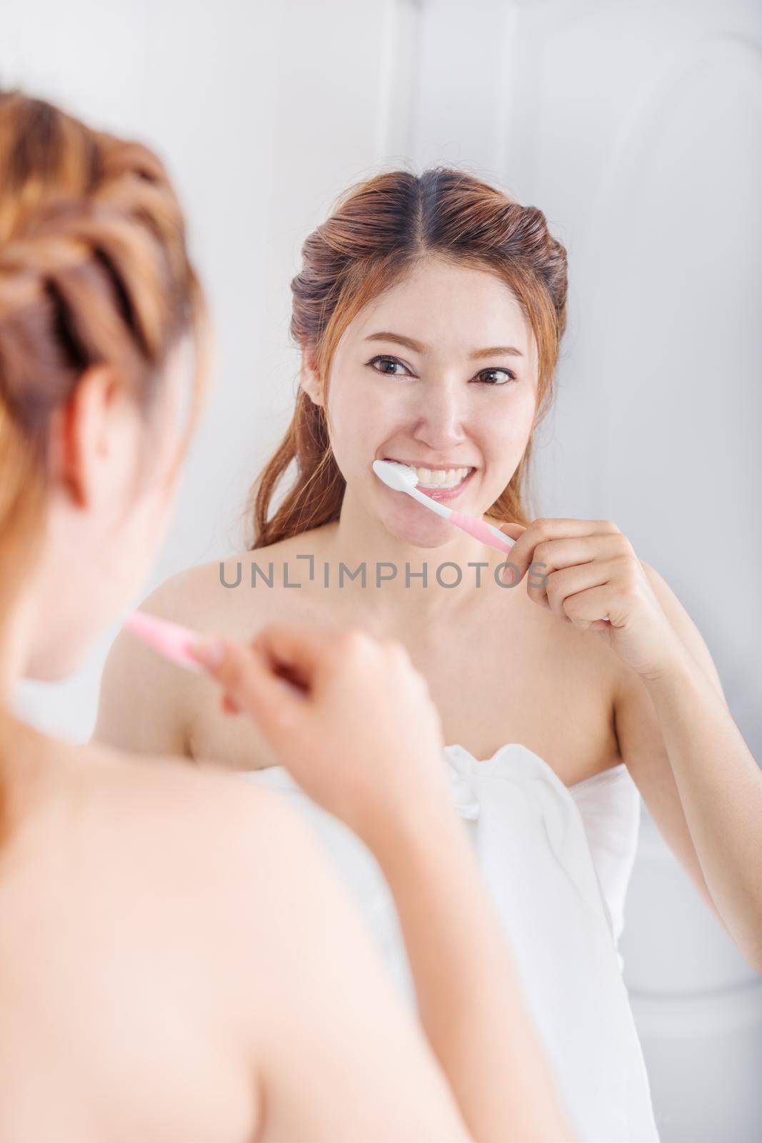 woman in bath towel brushing teeth with mirror in bathroom by geargodz